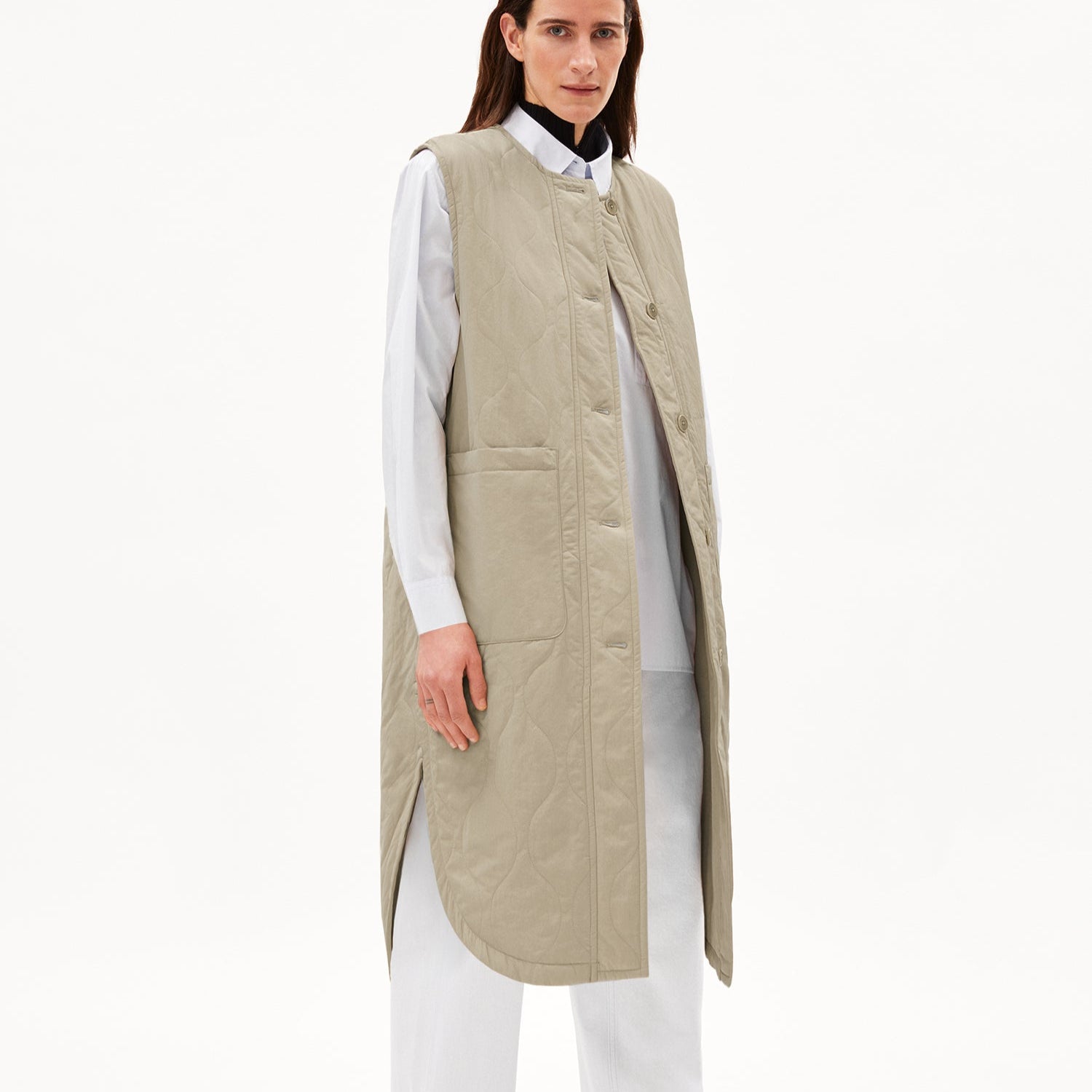 Person in beige Steppweste über weißem Hemd vor weißem Hintergrund.