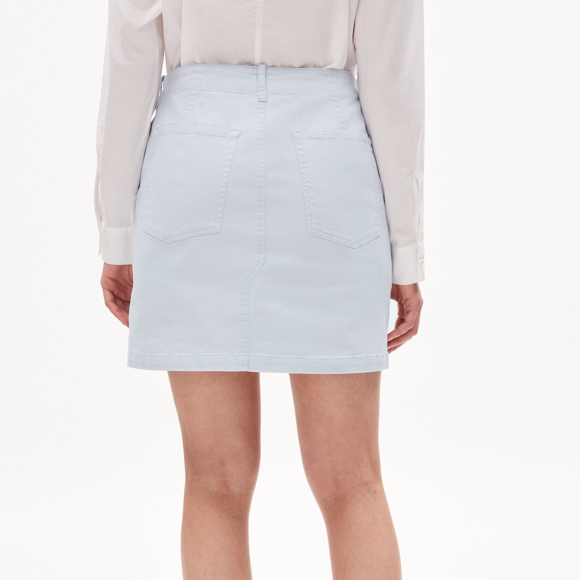 Eine Person trägt einen hellblauen Jeansrock und ein weißes Hemd, von hinten gesehen.