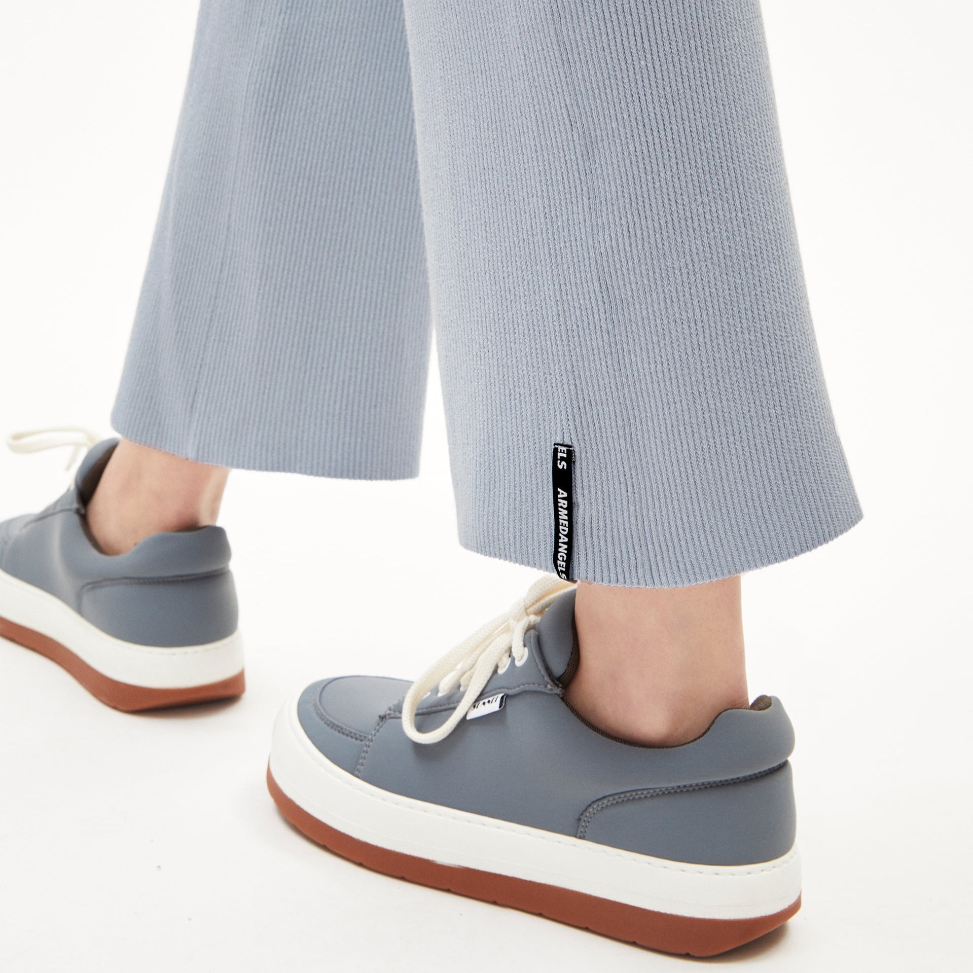 Graue Sneaker mit dicken weißen Sohlen und hellblauen, gerippten Hosenbeinen mit sichtbarem Label aus der Nähe.