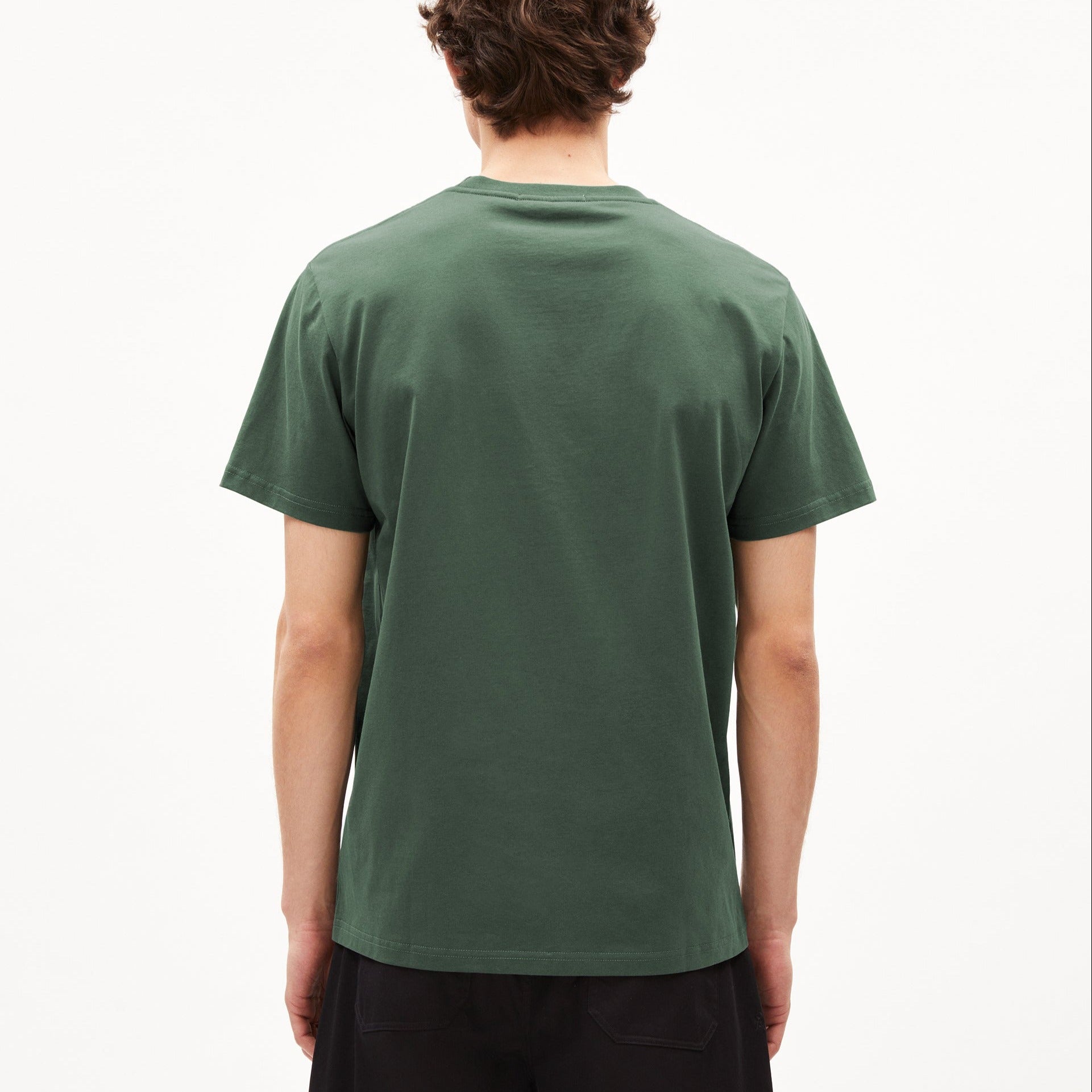 Rückansicht einer stehenden Person in einem dunkelgrünen T-Shirt vor einem weißen Hintergrund.