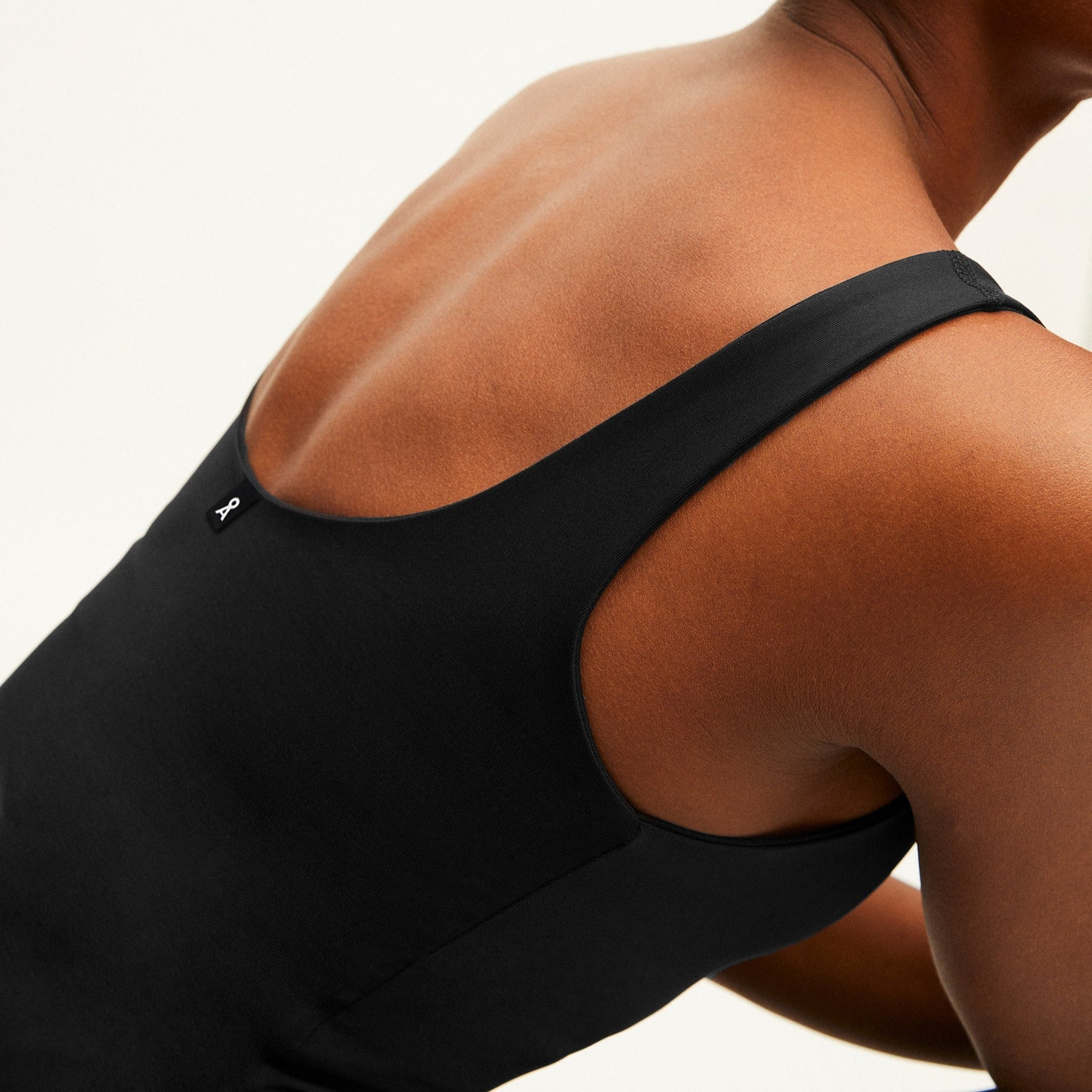 Eine Person trägt ein schwarzes Tanktop, der Rücken ist teilweise sichtbar.