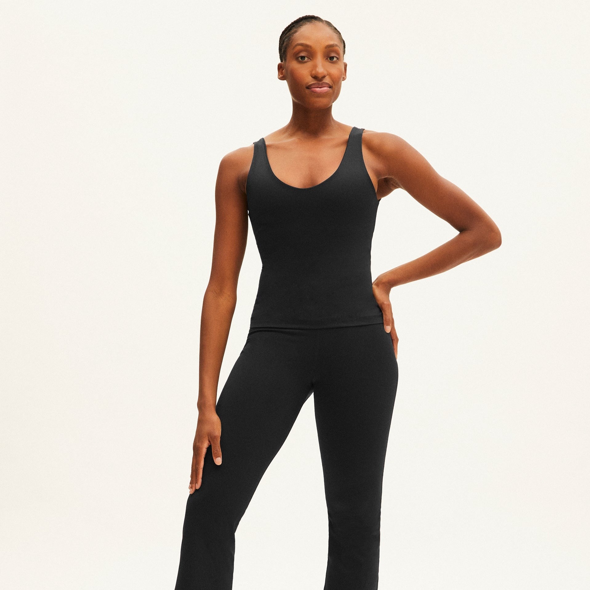 Eine Frau in schwarzer Sportbekleidung steht vor einem neutralen Hintergrund und lächelt leicht.