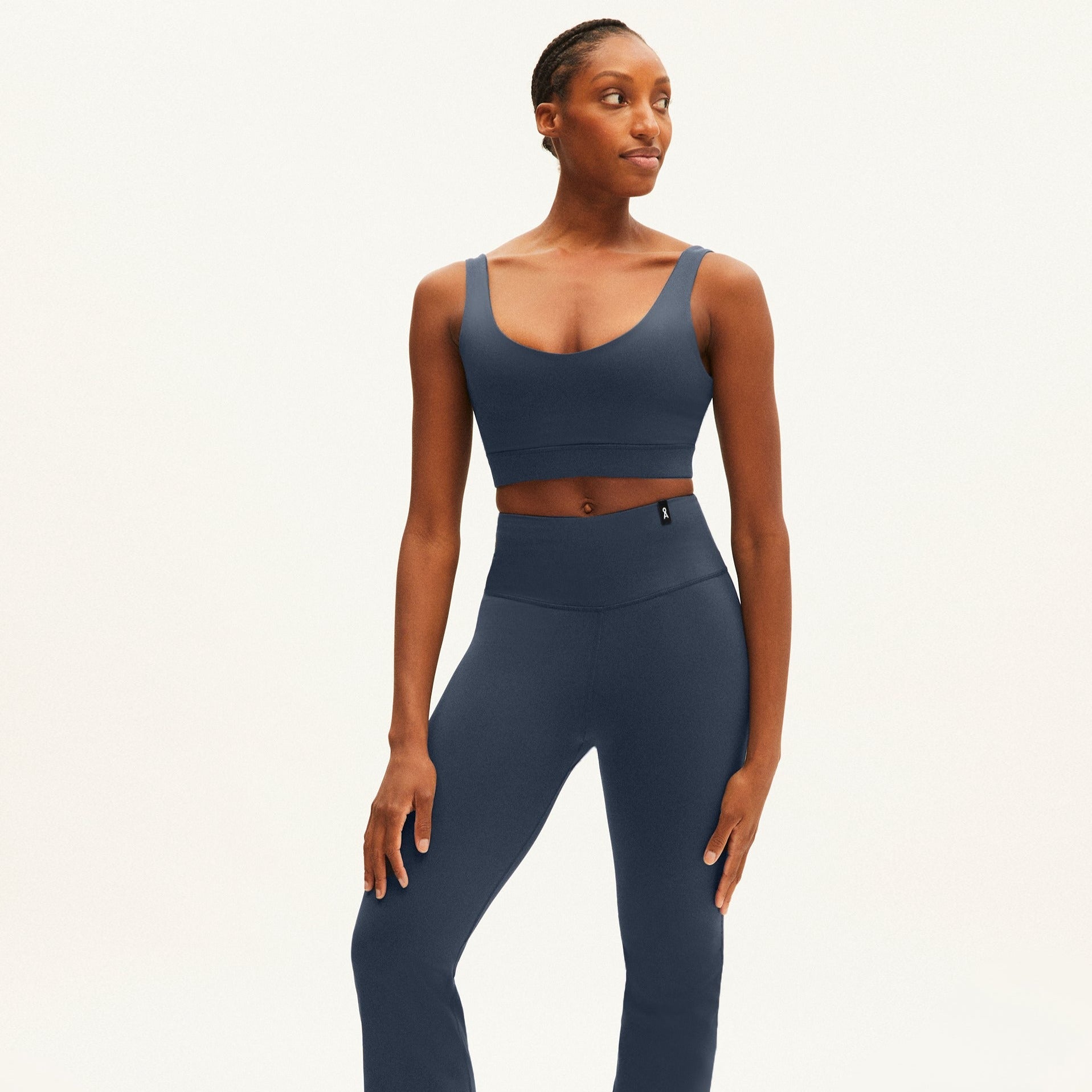 Frau in einem dunkelblauen Trainingsoutfit steht vor einem hellen Hintergrund und schaut zur Seite.