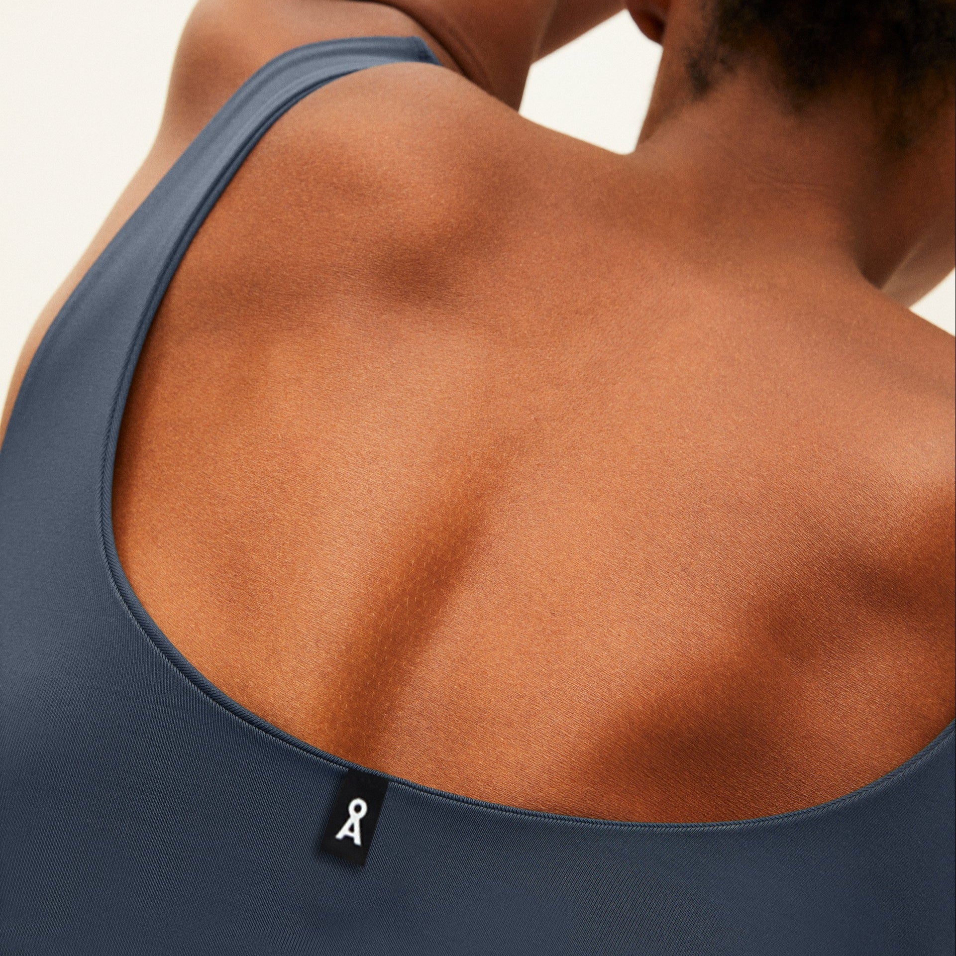 Rückansicht eines Oberkörpers in einem dunkelblauen ärmellosen Oberteil mit einem kleinen Etikett am Ausschnitt.