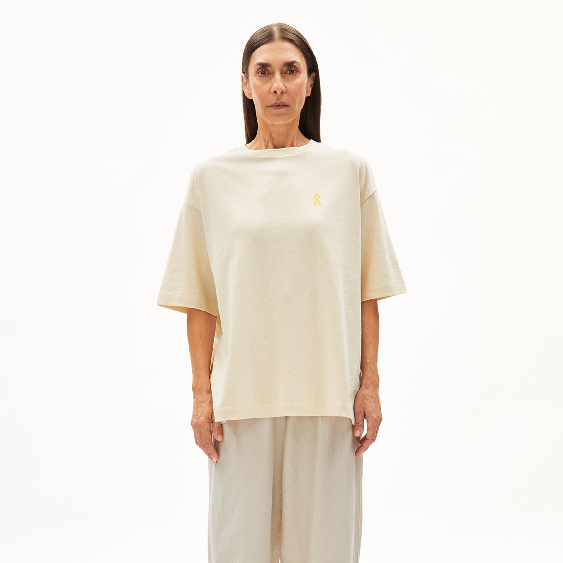 Person in beige T-Shirt und Hose steht vor weißem Hintergrund.