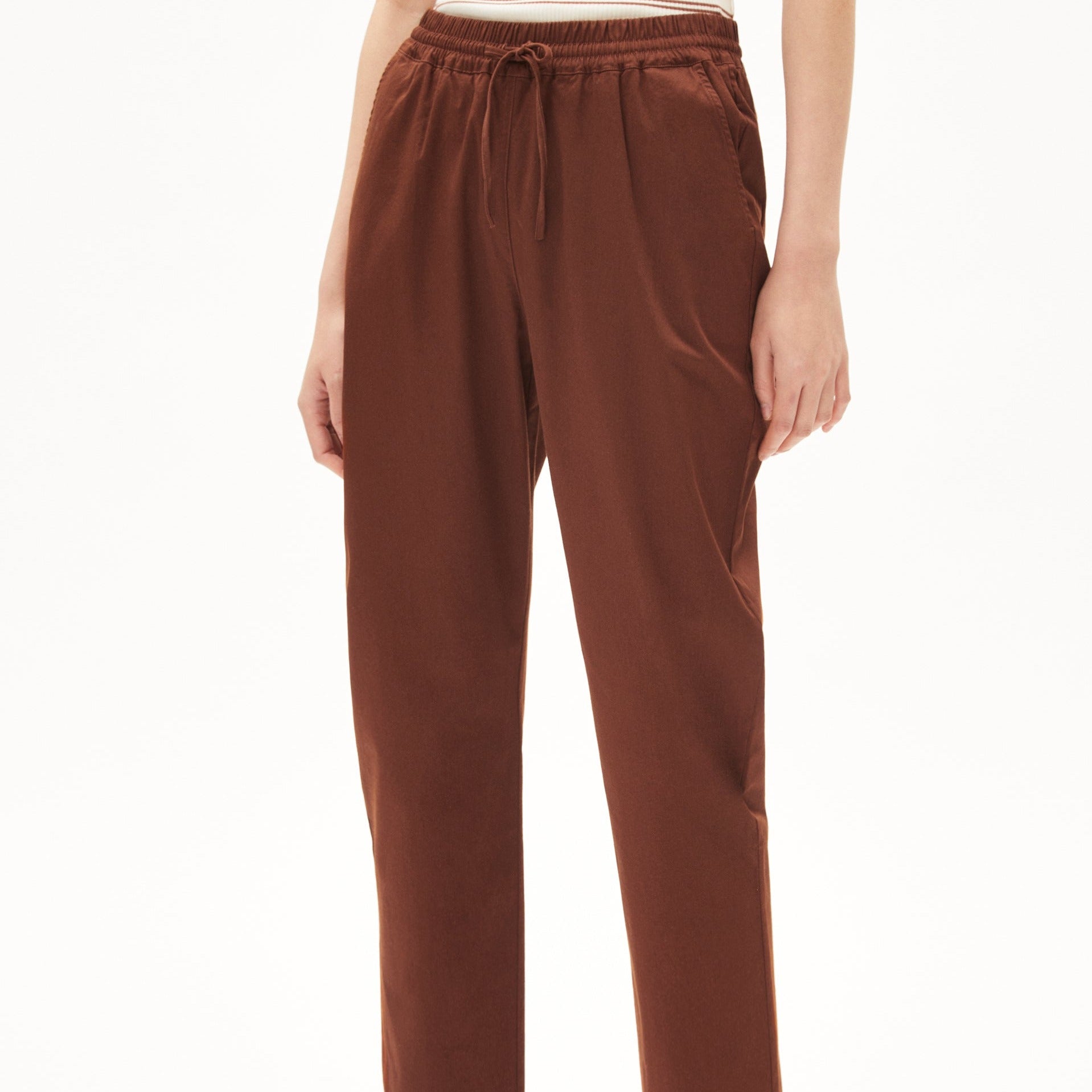 Person trägt braune Hose mit elastischem Bund und Kordelzug vor einem weißen Hintergrund.
