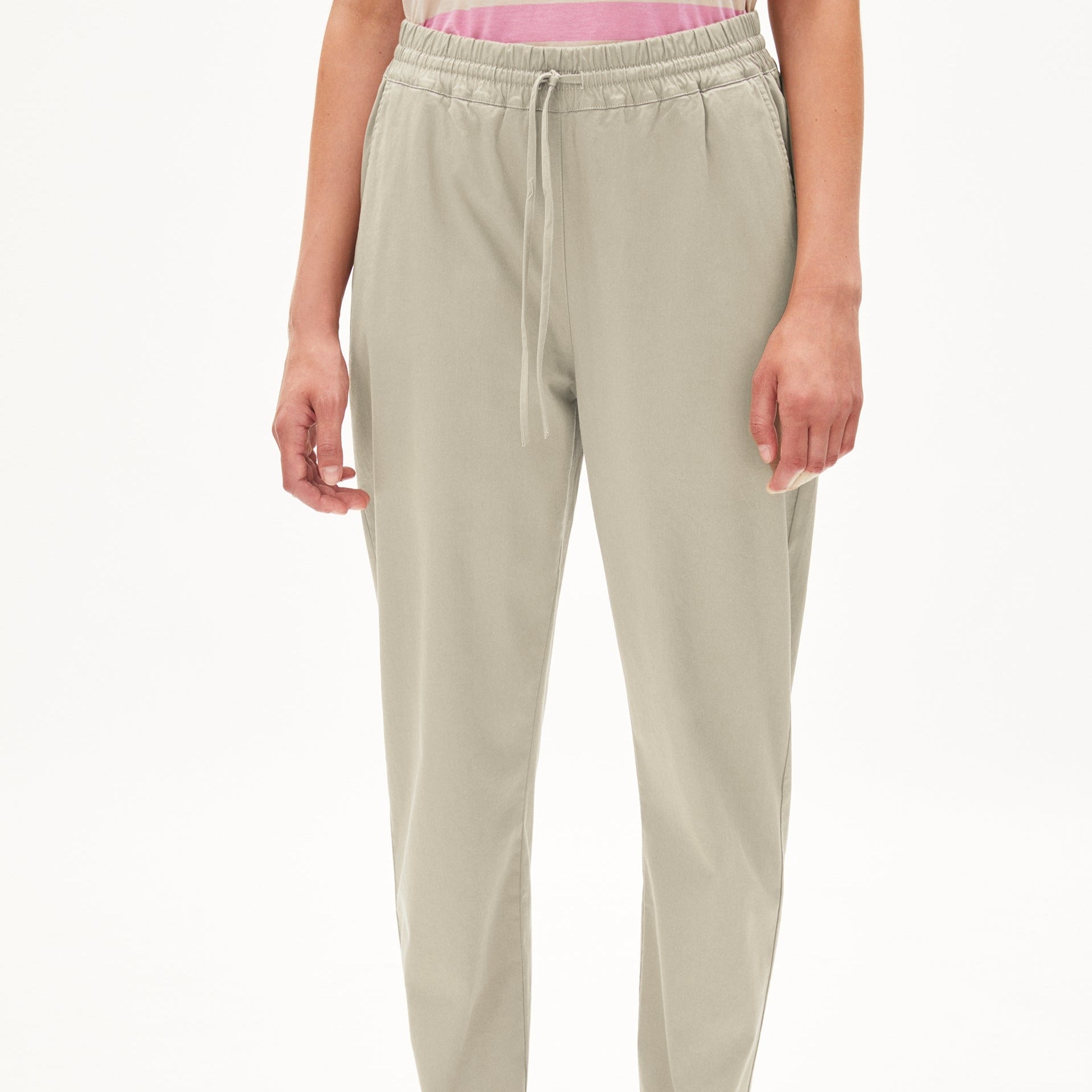 Person trägt eine beige Jogginghose und ein rosa gestreiftes Oberteil vor weißem Hintergrund.