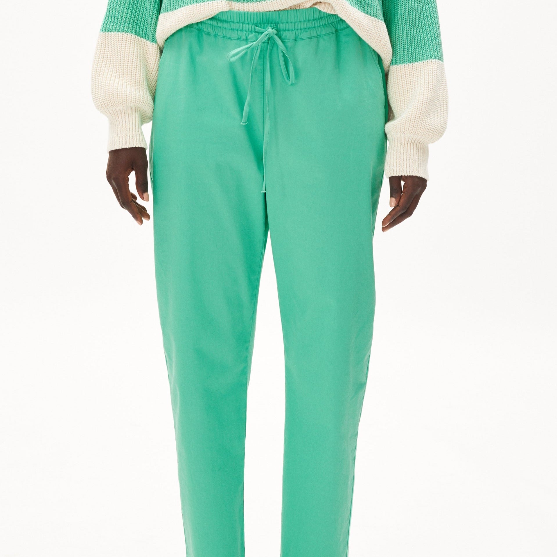 Person trägt grüne Jogginghose und gestreiften Pullover, Fokus auf unteren Rumpfbereich bis Oberschenkel.