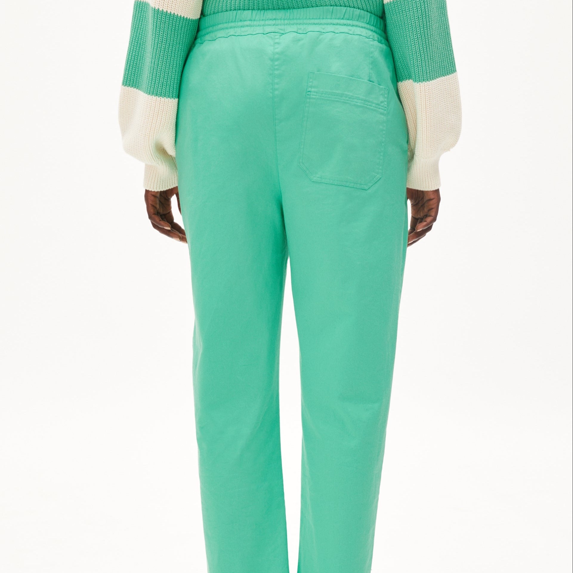 Eine Person trägt eine grüne Hose und einen grünen Pullover mit weißen Streifen, von hinten gesehen.