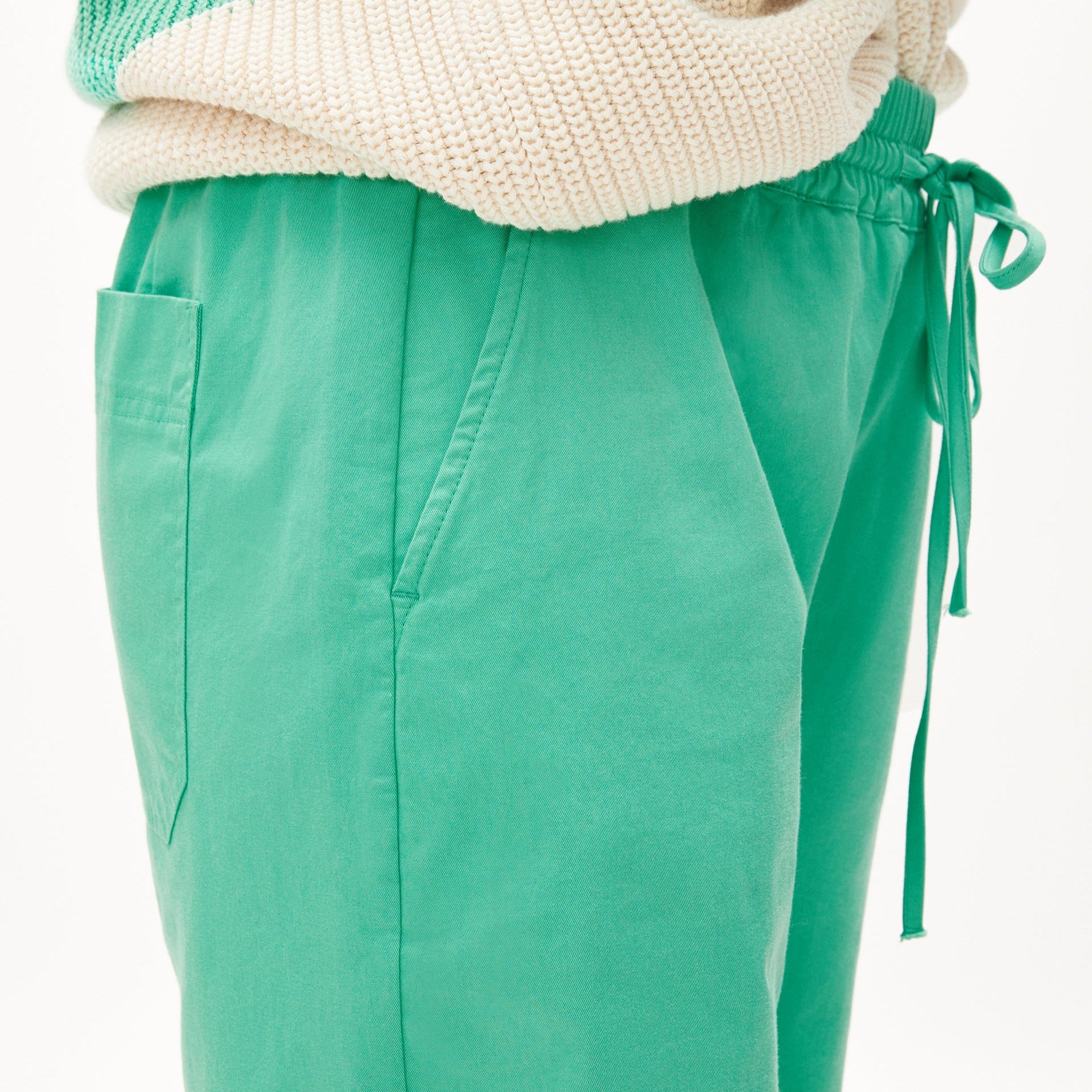 Nahaufnahme einer Person in grüner Hose mit Kordelzug und beigem Strickpullover.