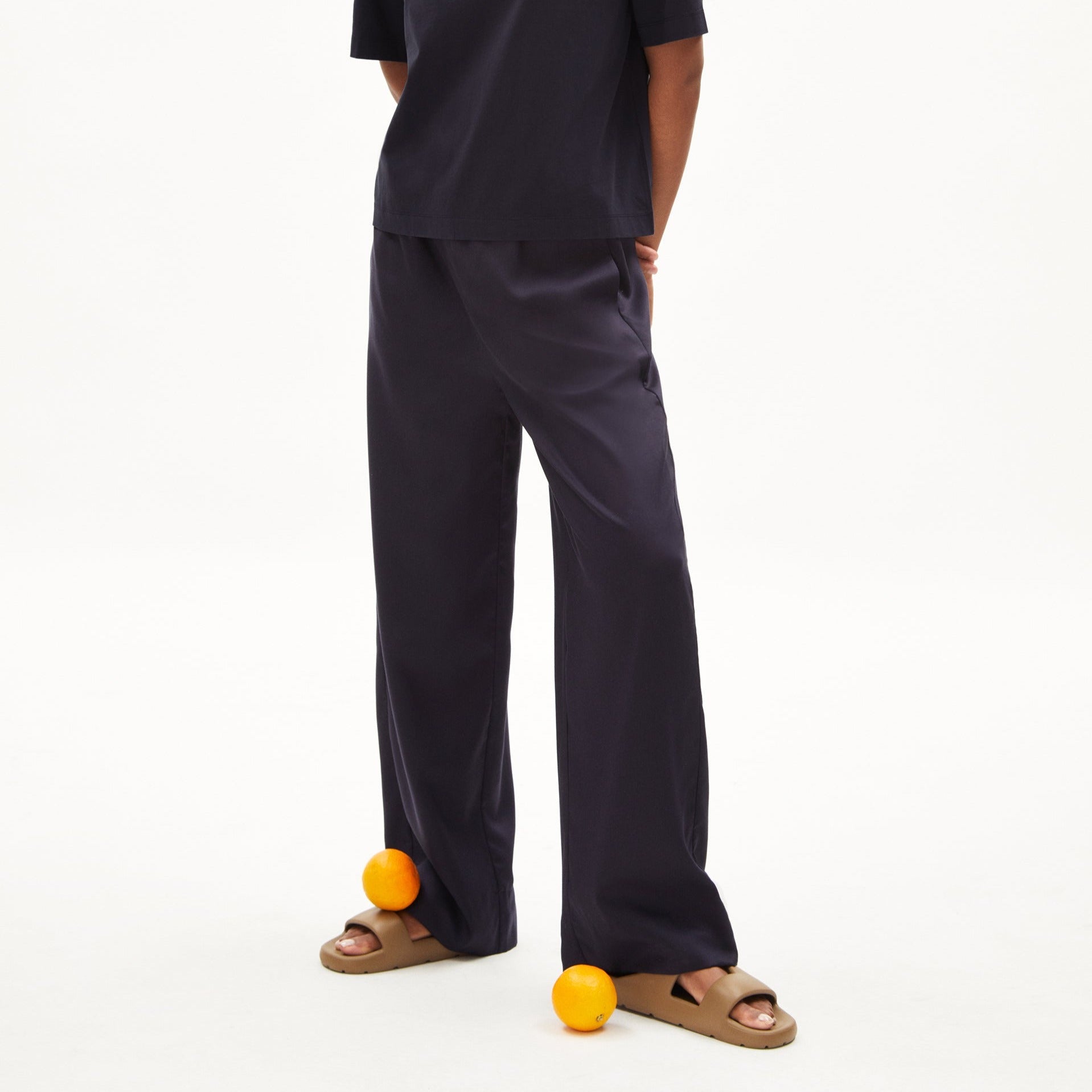 Eine Person in dunkelblauer Kleidung steht mit Orangen vor den Füßen auf dem Boden.