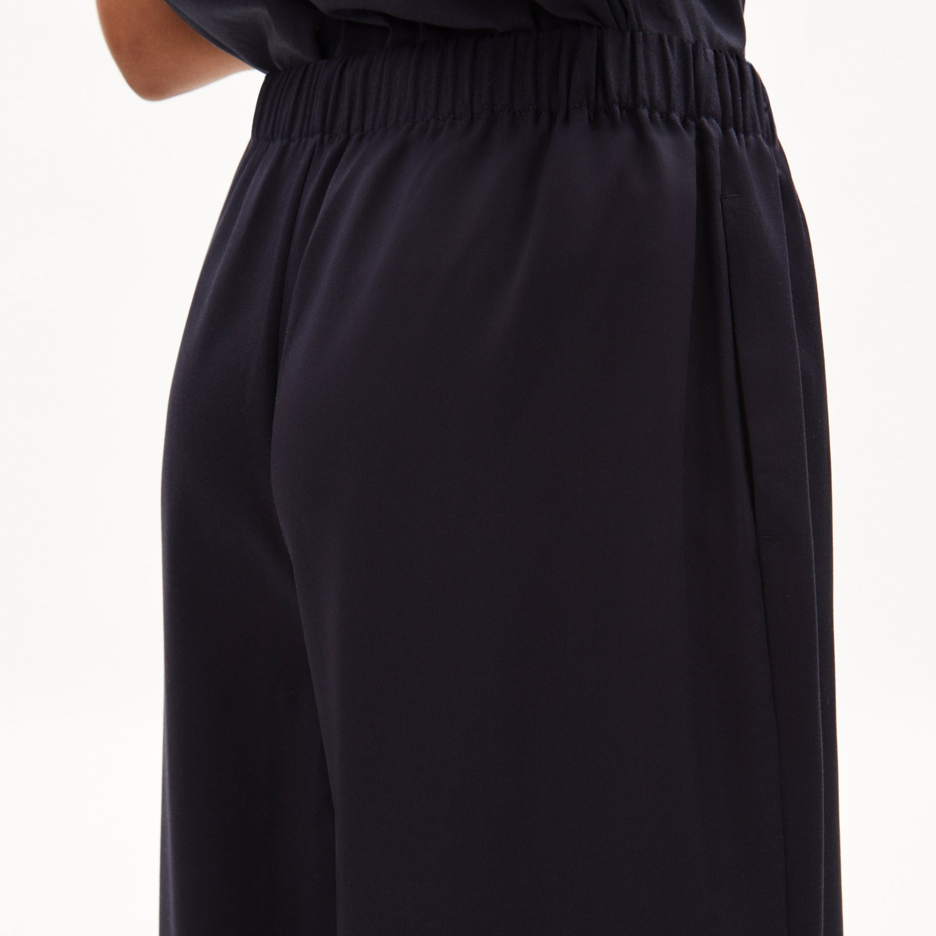 Nahaufnahme einer Person in einer dunkelblauen Hose mit elastischem Bund, von der Hüfte bis zum Oberschenkelbereich.