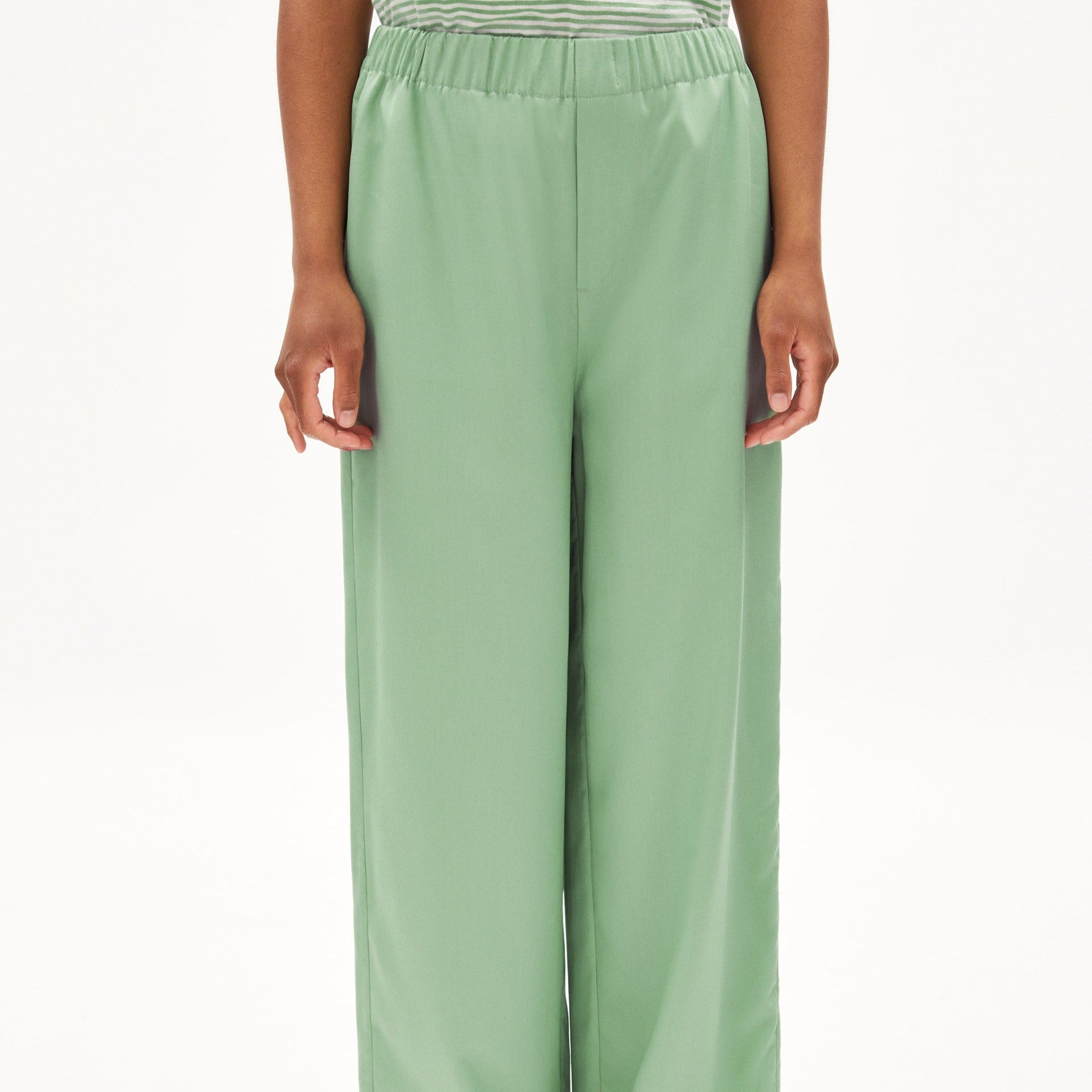 Person in einem gestreiften Oberteil und grüner, lockerer Hose, von der Hüfte abwärts gezeigt.