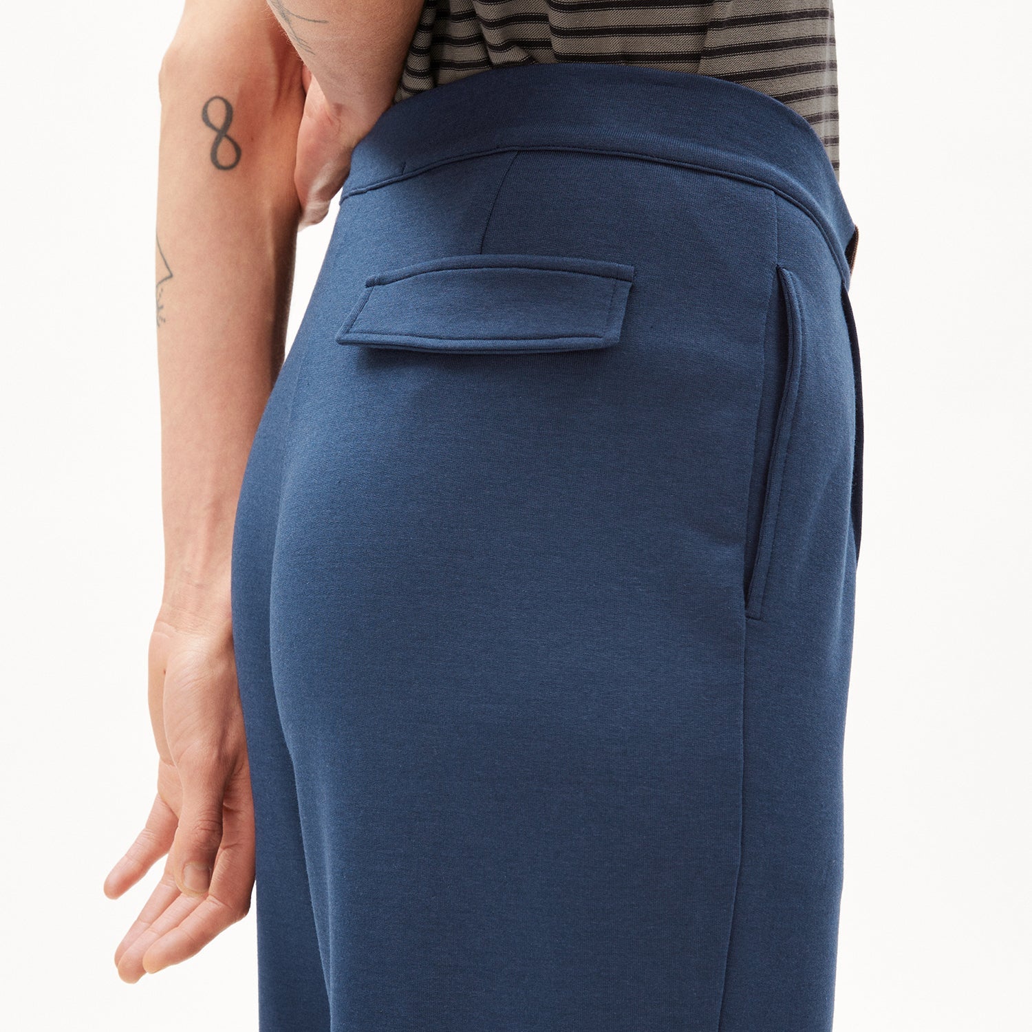 Person trägt eine blaue Hose mit einer Gesäßtasche, Arm mit Tattoos sichtbar.