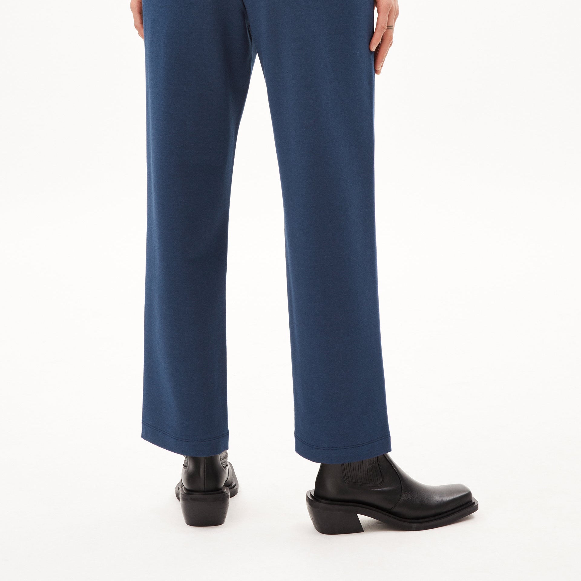 Person in blauer Hose und schwarzen Stiefeletten steht auf hellem Hintergrund.