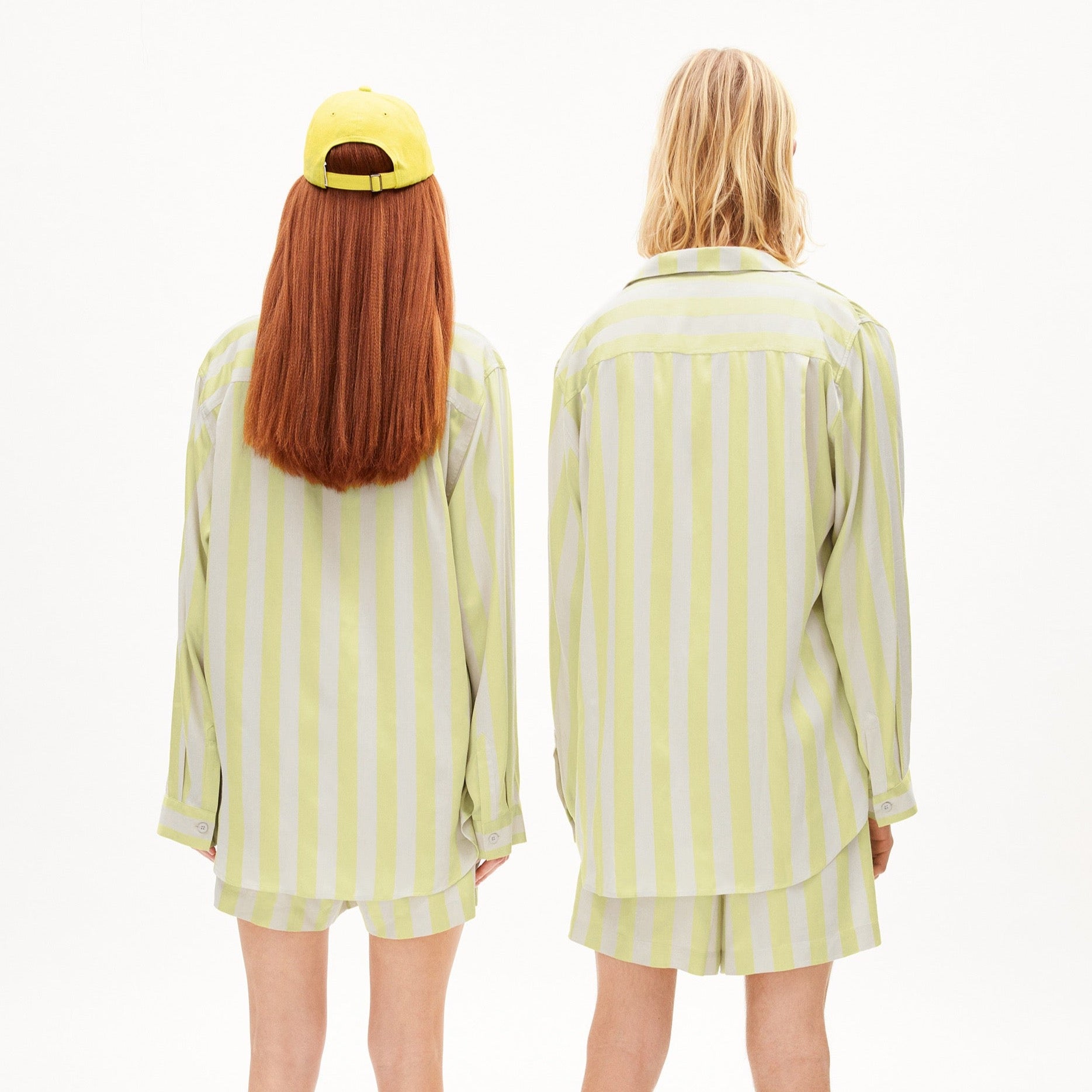 Zwei Personen von hinten in gestreiften Hemden und gelben Shorts, eine trägt eine gelbe Kappe.
