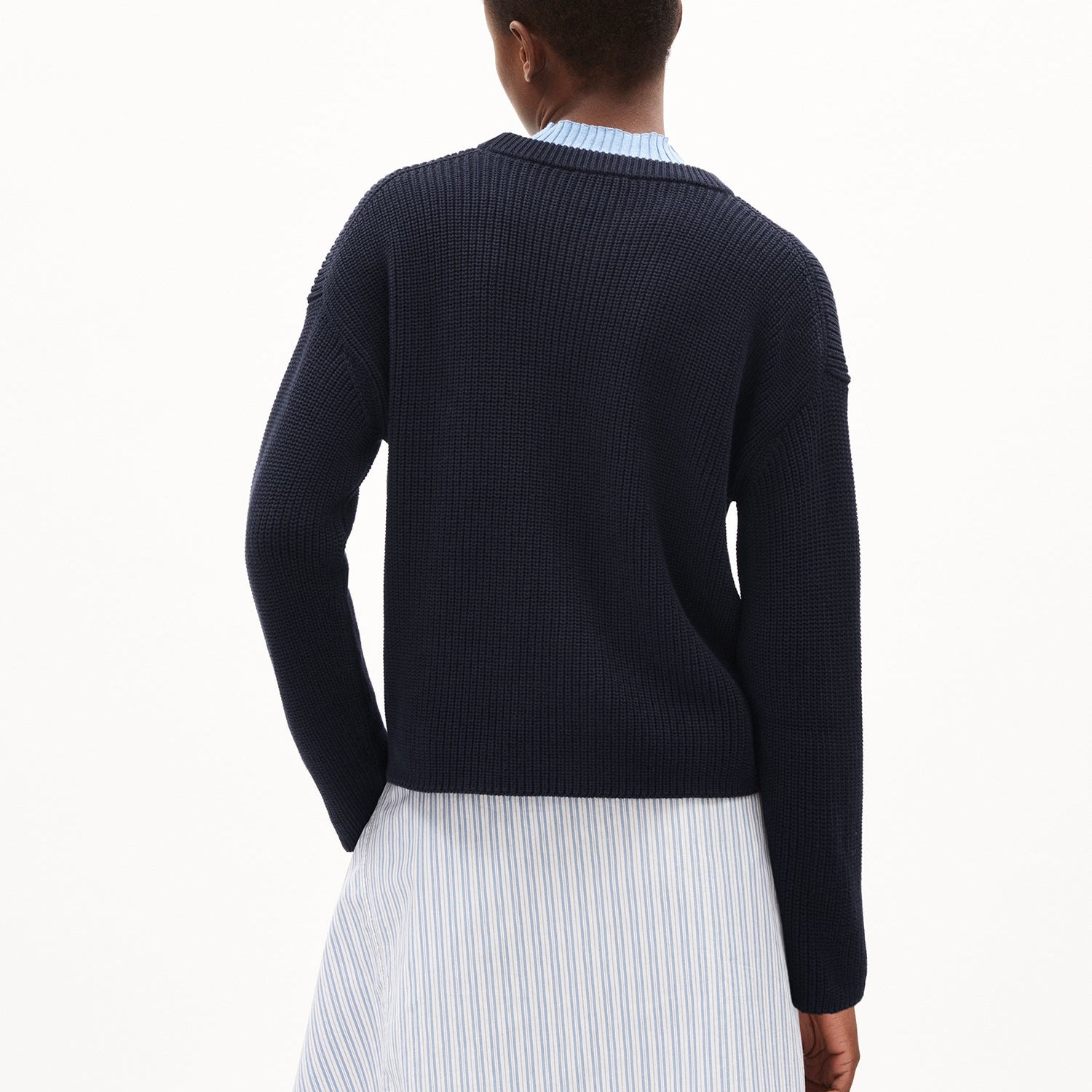 Person von hinten in einem dunkelblauen Pullover und einem gestreiften Hemd.