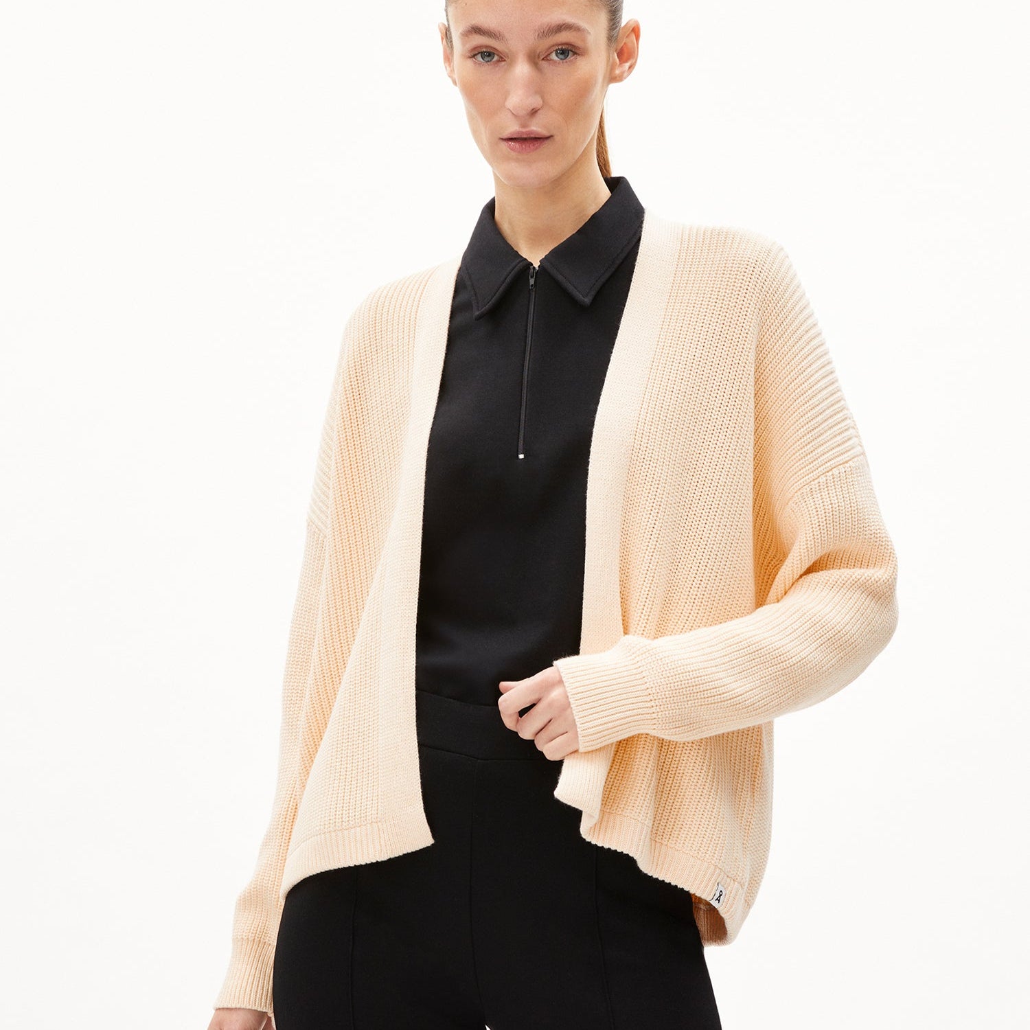 Person in cream cardigan and black shirt, posing against white background.