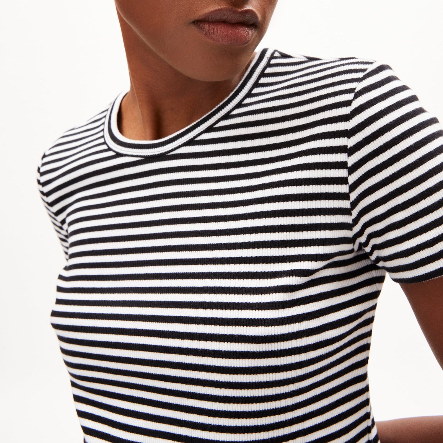Person in einem schwarz-weiß gestreiften T-Shirt vor weißem Hintergrund, mit Fokus auf den Oberkörper.