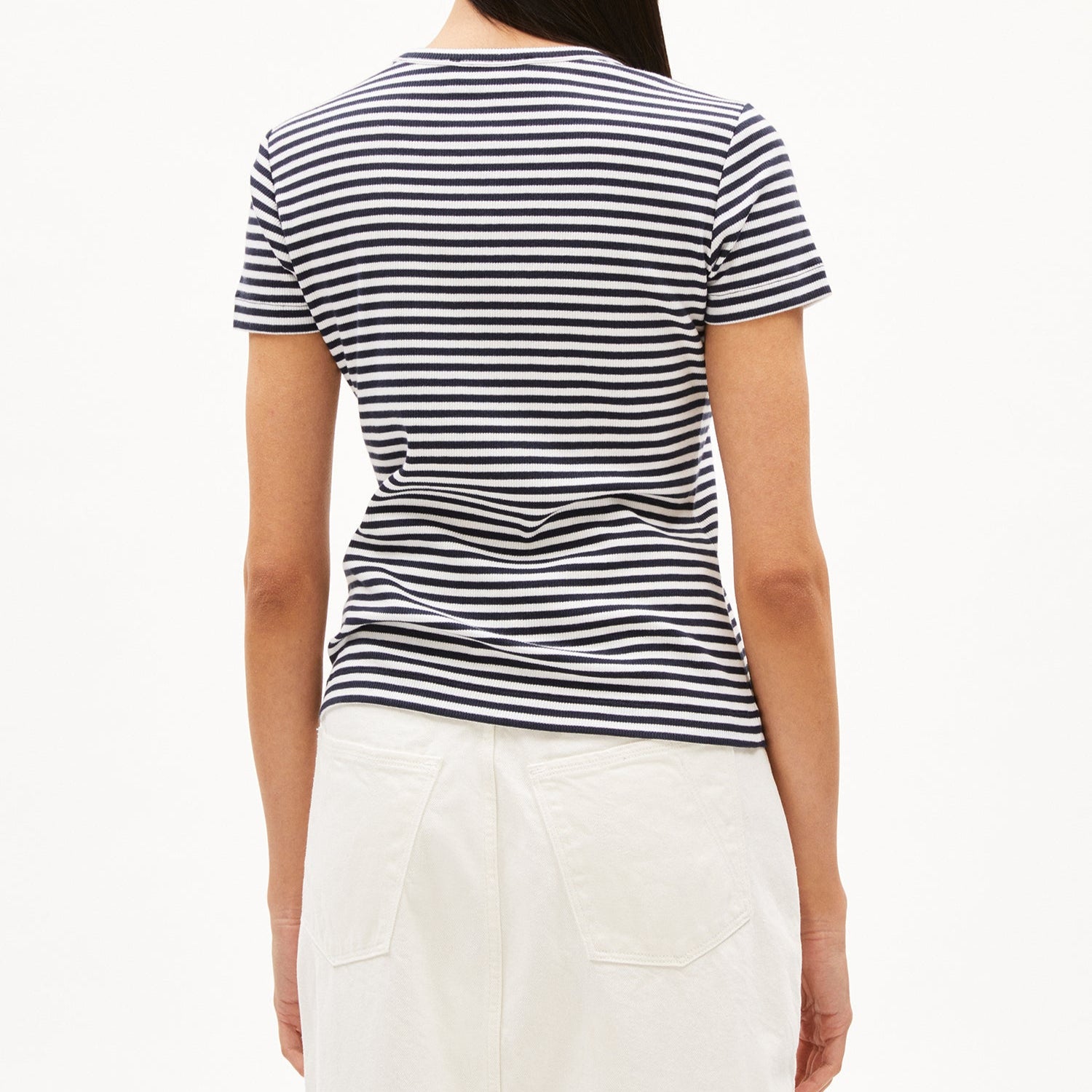 Frau von hinten in gestreiftem T-Shirt und weißem Rock vor weißem Hintergrund.