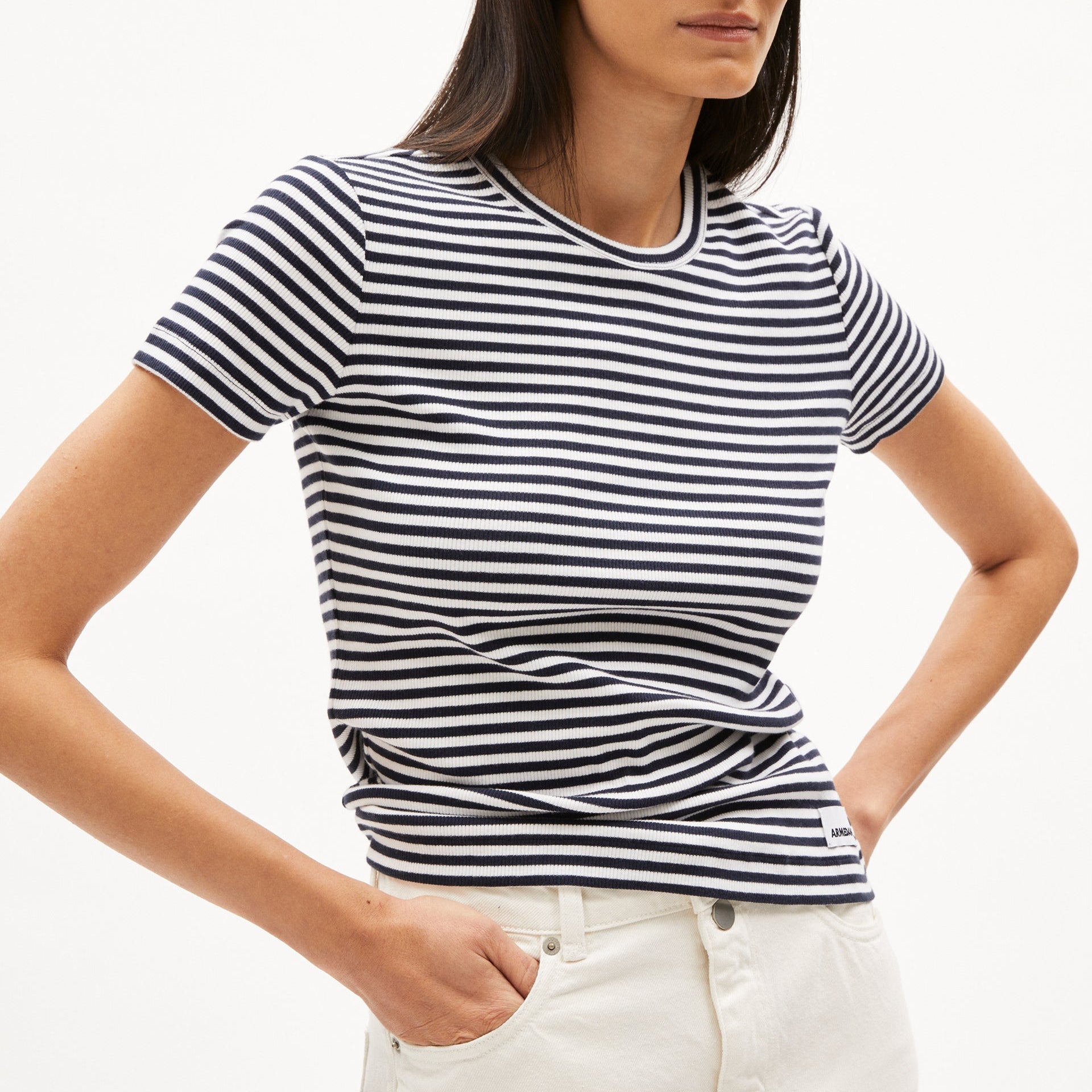 Frau in einem gestreiften T-Shirt und weißen Hosen, mit einer Hand in der Tasche.