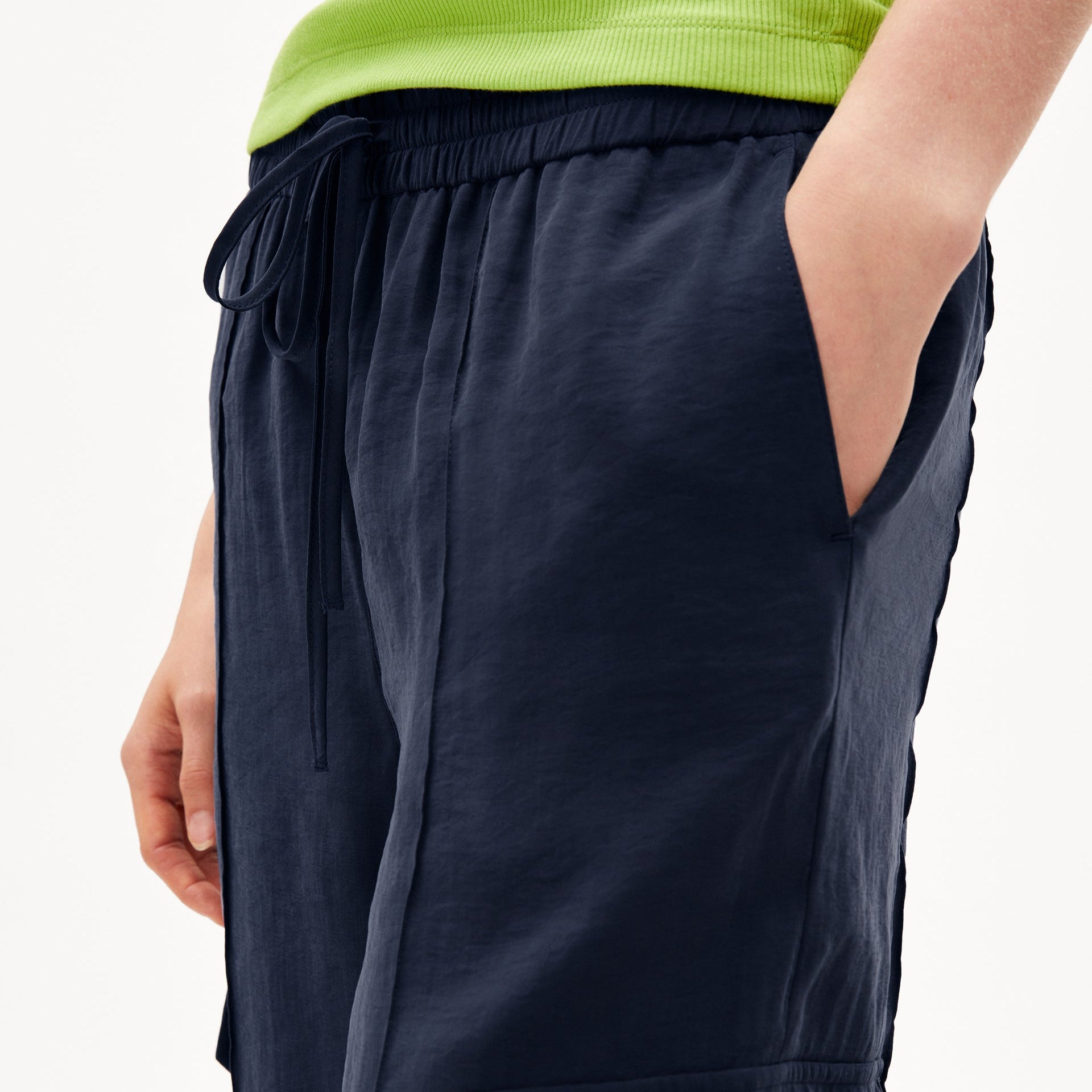 Person trägt eine dunkelblaue Hose mit elastischem Bund und Händen in den Taschen, kombiniert mit einem grünen Oberteil.