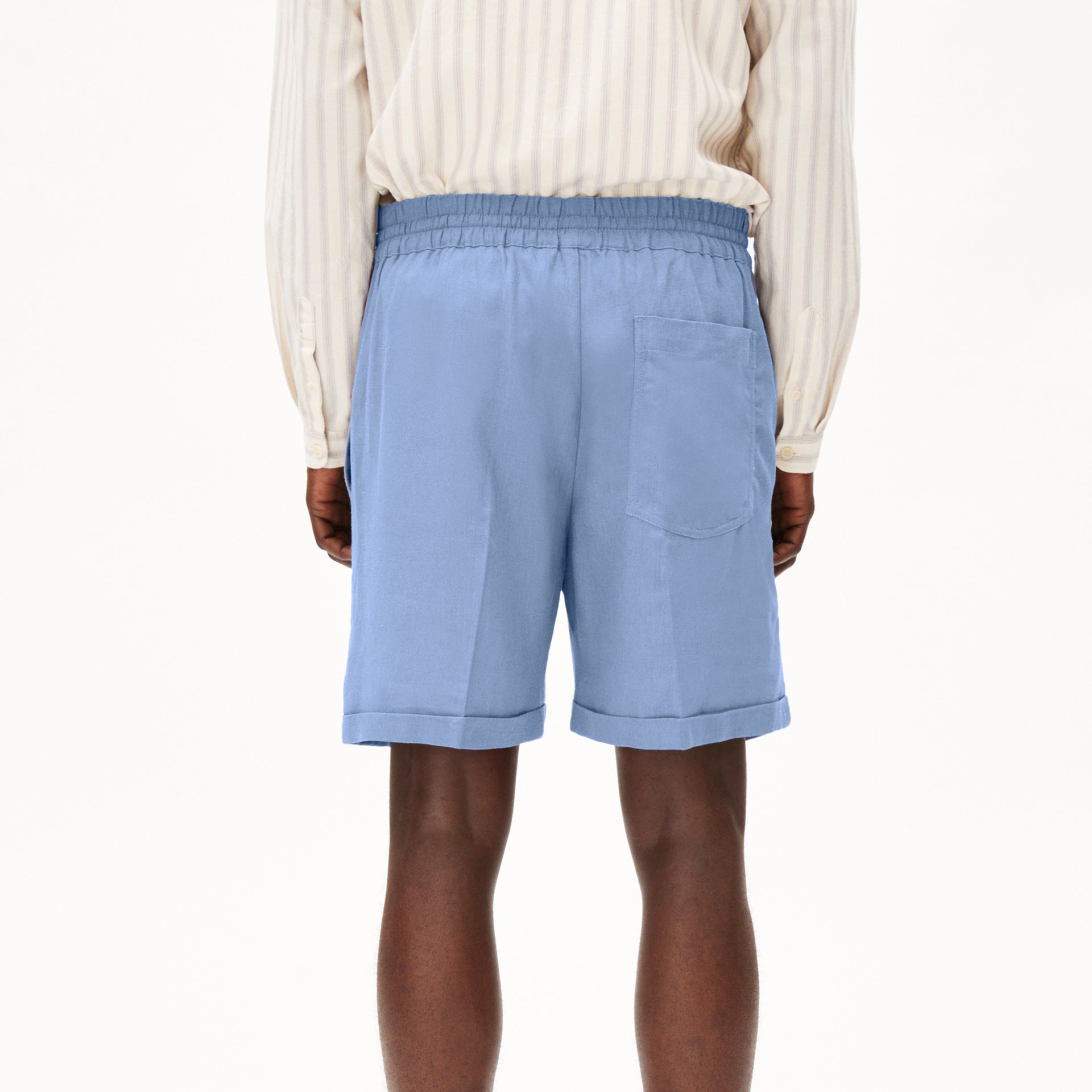Person in gestreiftem Hemd und blauen Shorts von hinten vor weißem Hintergrund.
