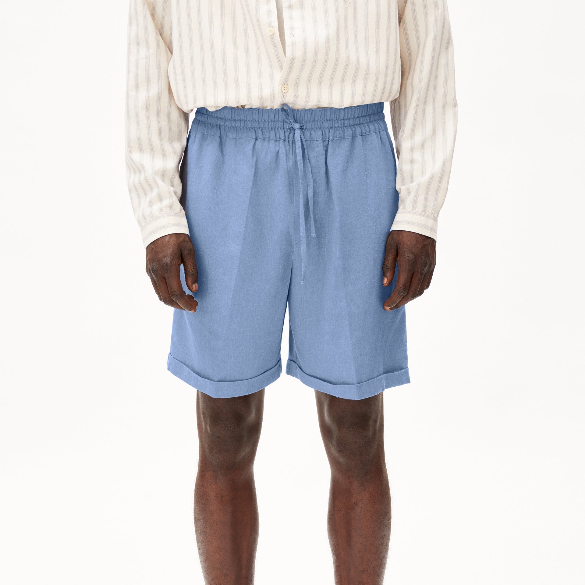 Person trägt ein gestreiftes Hemd und hellblaue Shorts mit Kordelzug vor weißem Hintergrund.