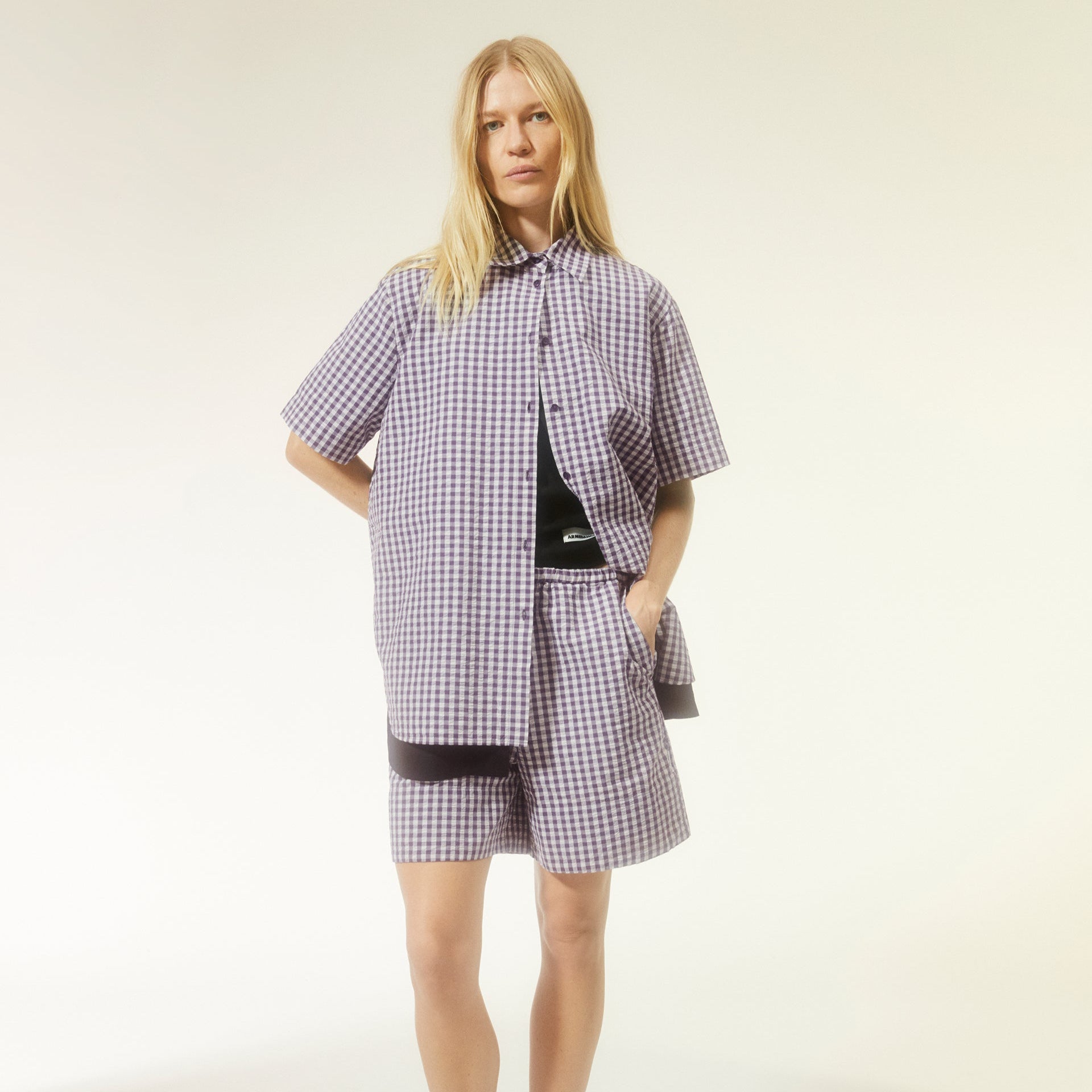 Frau in lila-kariertem Hemd und Shorts mit gelbem Hintergrund.
