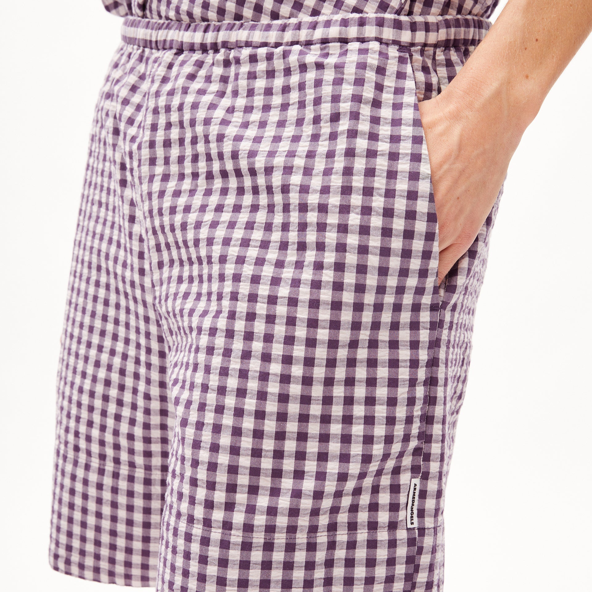 Person trägt eine lila-weiß karierte Hose, die Hand locker in der Tasche.