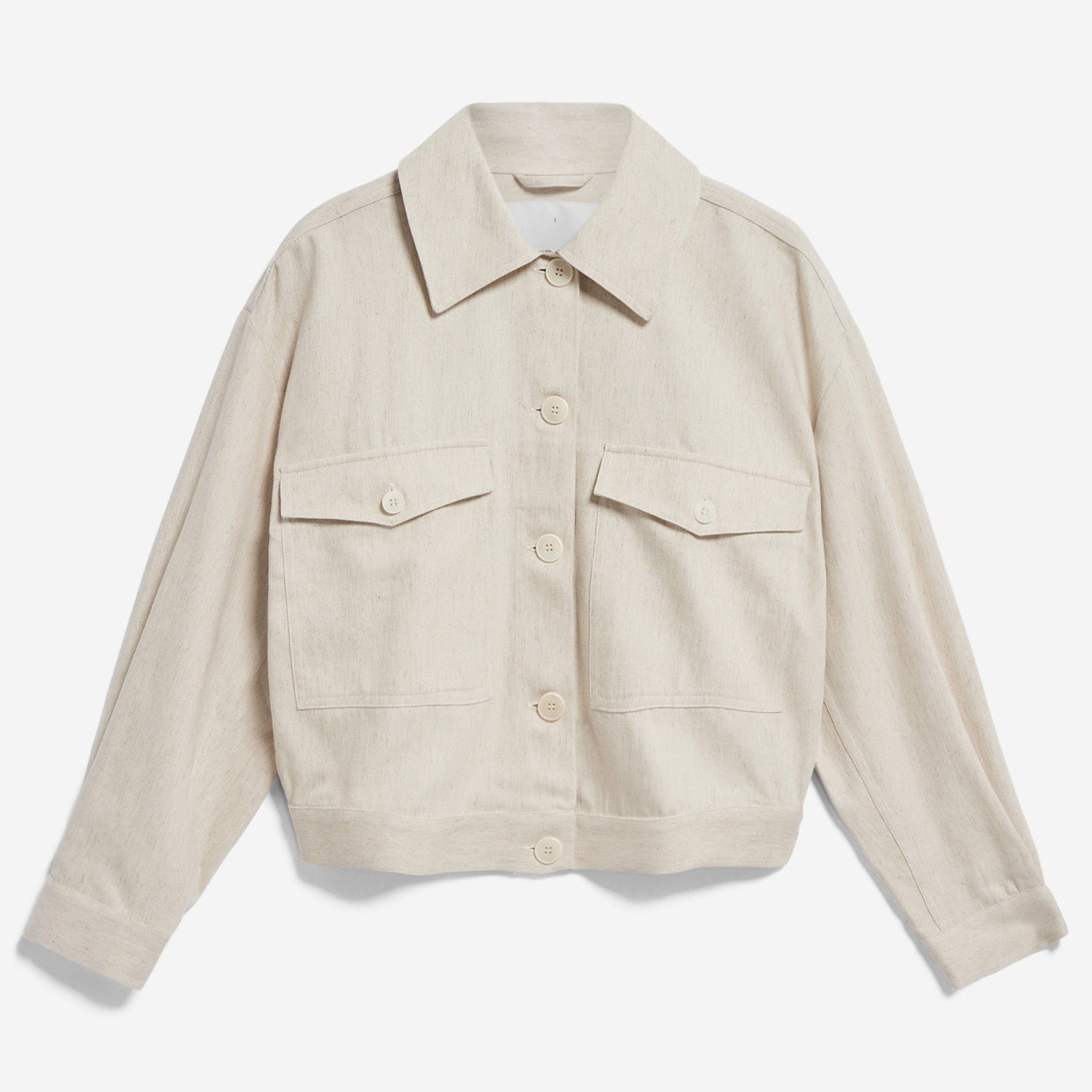 Beige Jacke mit Knopfleiste und zwei Brusttaschen, mit Kragen und langen Ärmeln, auf weißem Hintergrund.