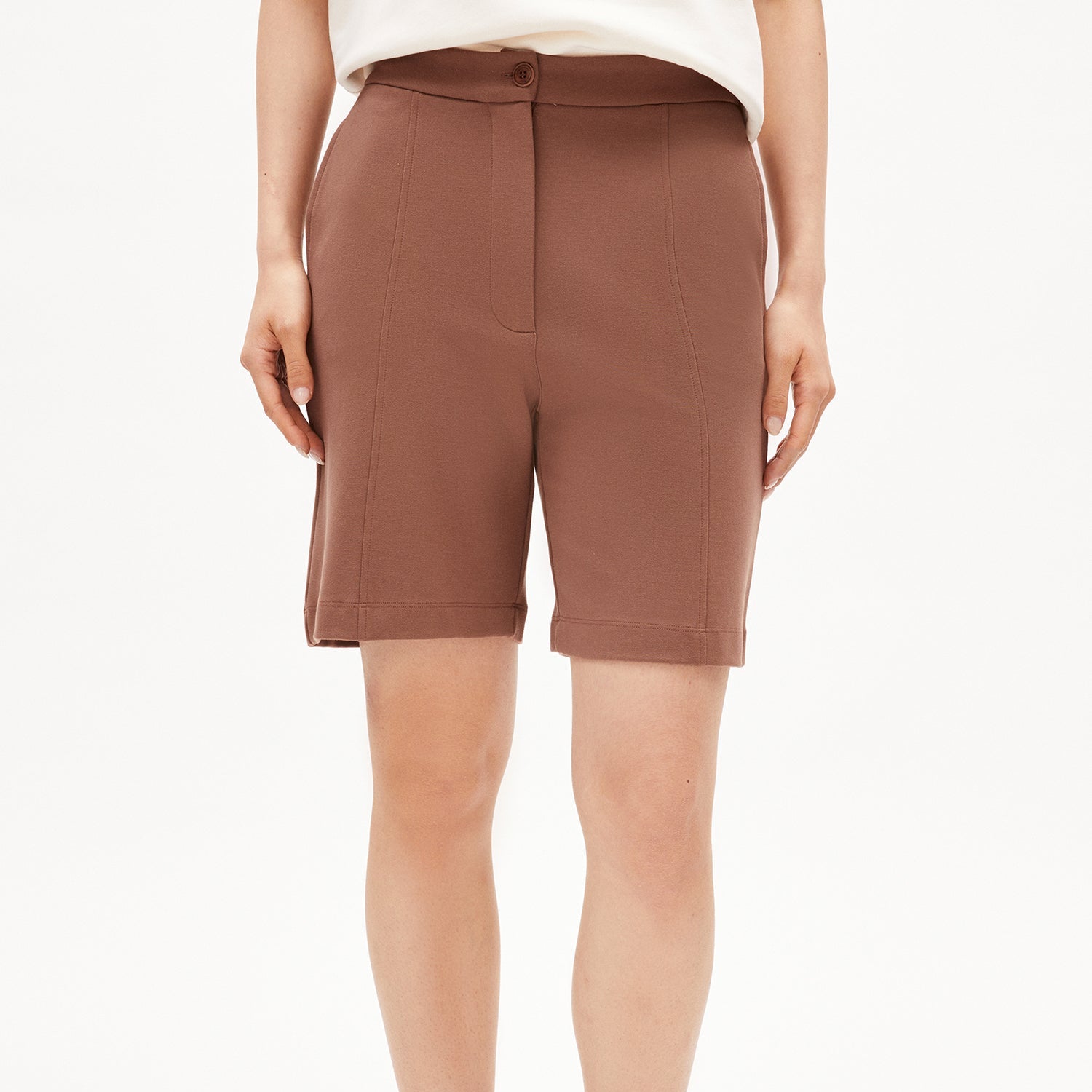 Person trägt braune Shorts und ein weißes T-Shirt vor einem weißen Hintergrund.