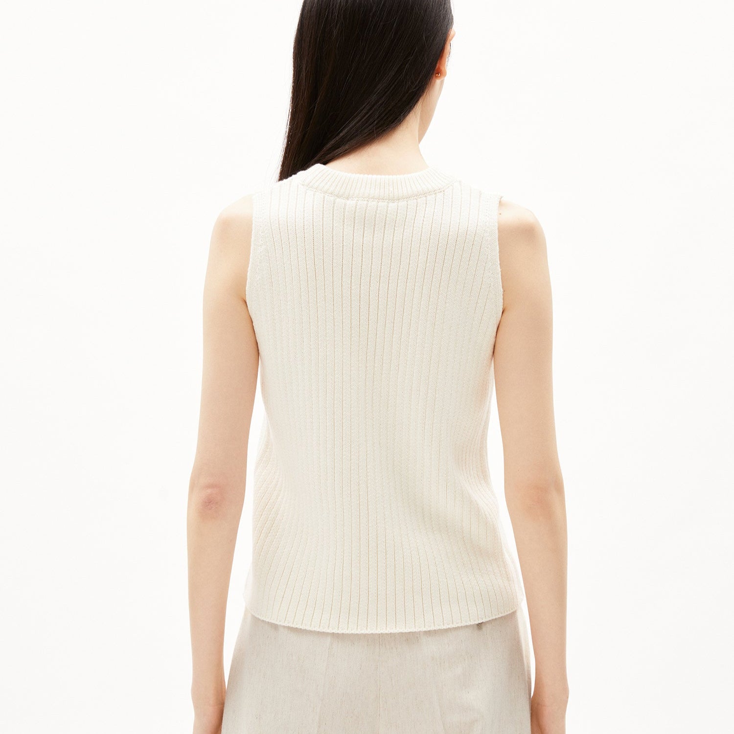 Eine Frau mit langen Haaren trägt einen ärmellosen, cremefarbenen, gerippten Pullover, von hinten gesehen.