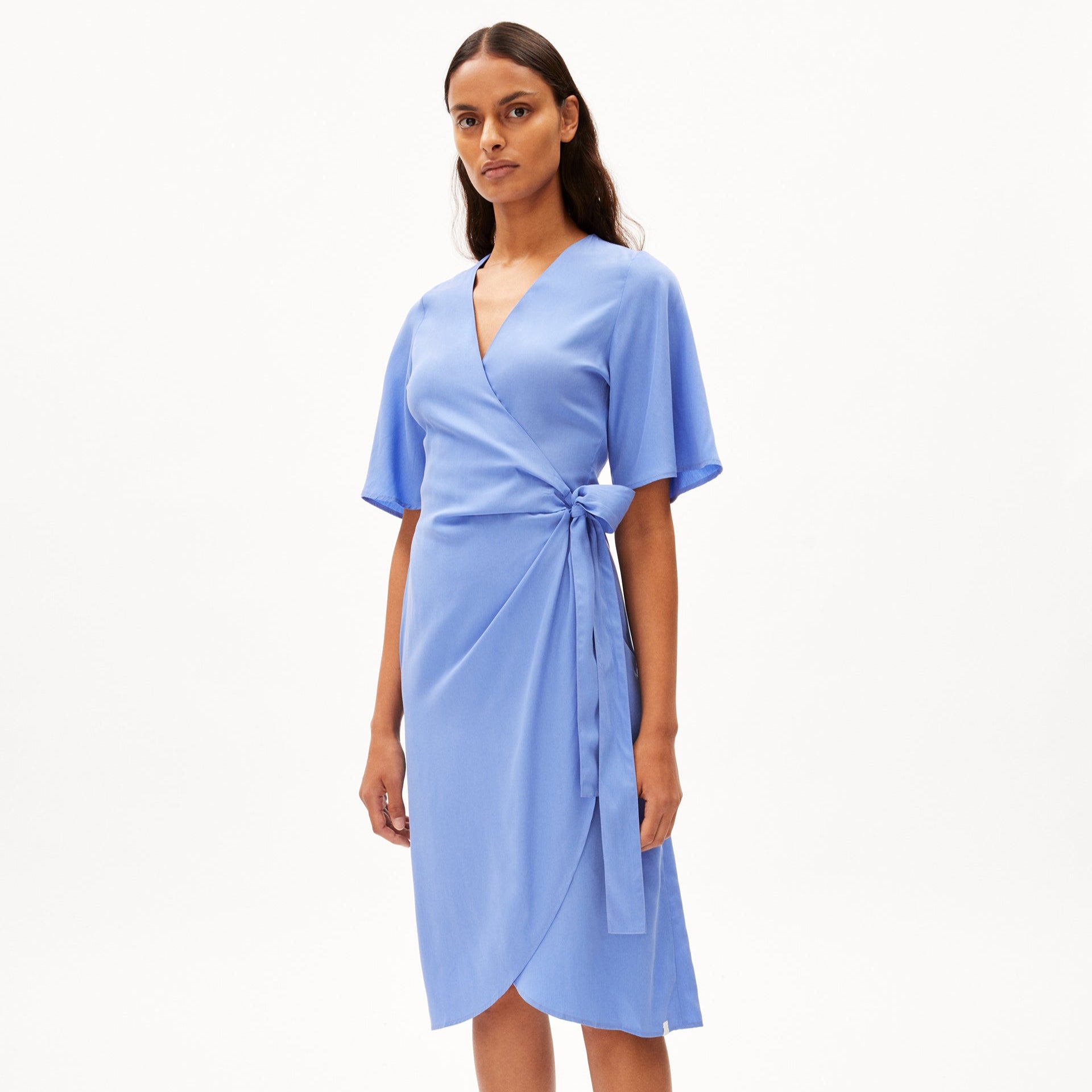 Eine Person trägt ein blaues Wickelkleid mit kurzen Ärmeln vor einem weißen Hintergrund.
