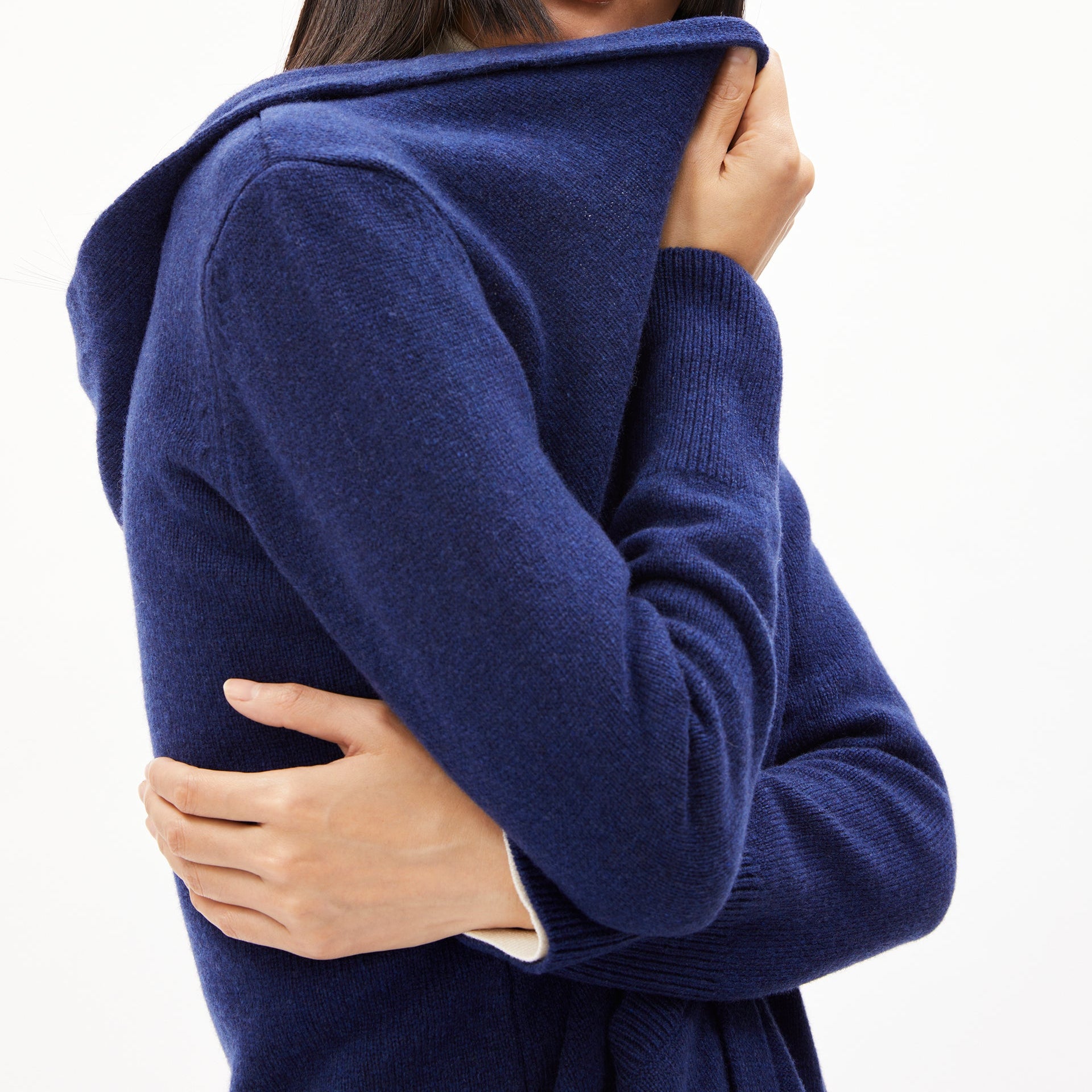Person wickelt sich in einen blauen Strickpullover ein, Hände halten den Stoff nah am Gesicht.