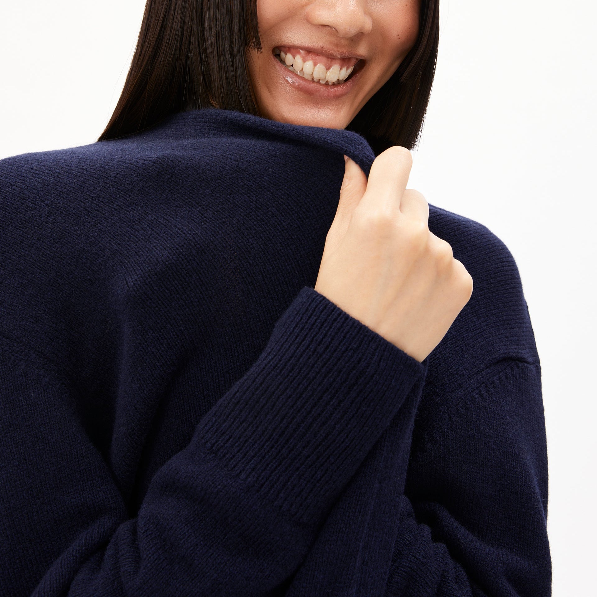 Person in a dark blue Pullover lächelt und hält den Kragen, Nahaufnahme von Gesicht und Schulter.
