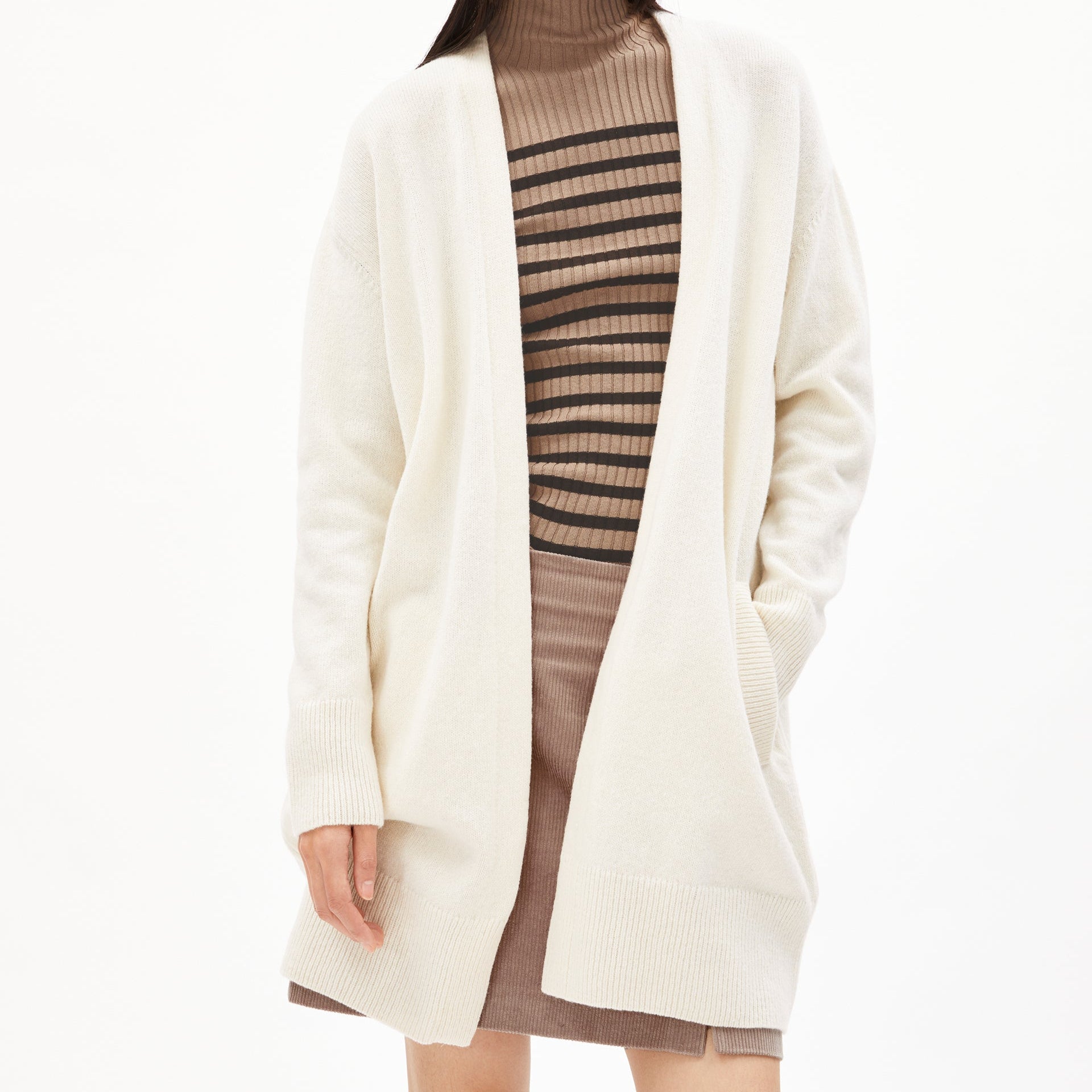 Person in beige Strickjacke über gestreiftem Rollkragenpullover und braunem Rock, vor weißem Hintergrund.