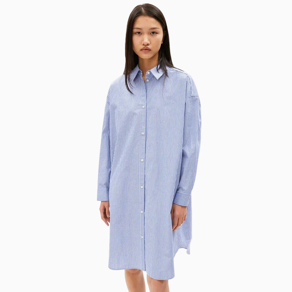 Eine Frau steht mit dem Gesicht nach vorne und trägt ein locker sitzendes, blau-weiß vertikal gestreiftes Hemdkleid mit langen Ärmeln. Der Hintergrund ist einfarbig weiß.