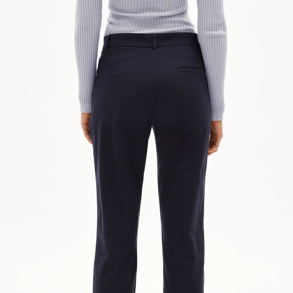 Eine Person, die eine marineblaue Hose mit geradem Bein, ein helles geripptes langärmeliges Oberteil und beigefarbene Schuhe trägt, wird von hinten vor einem schlichten weißen Hintergrund gezeigt.