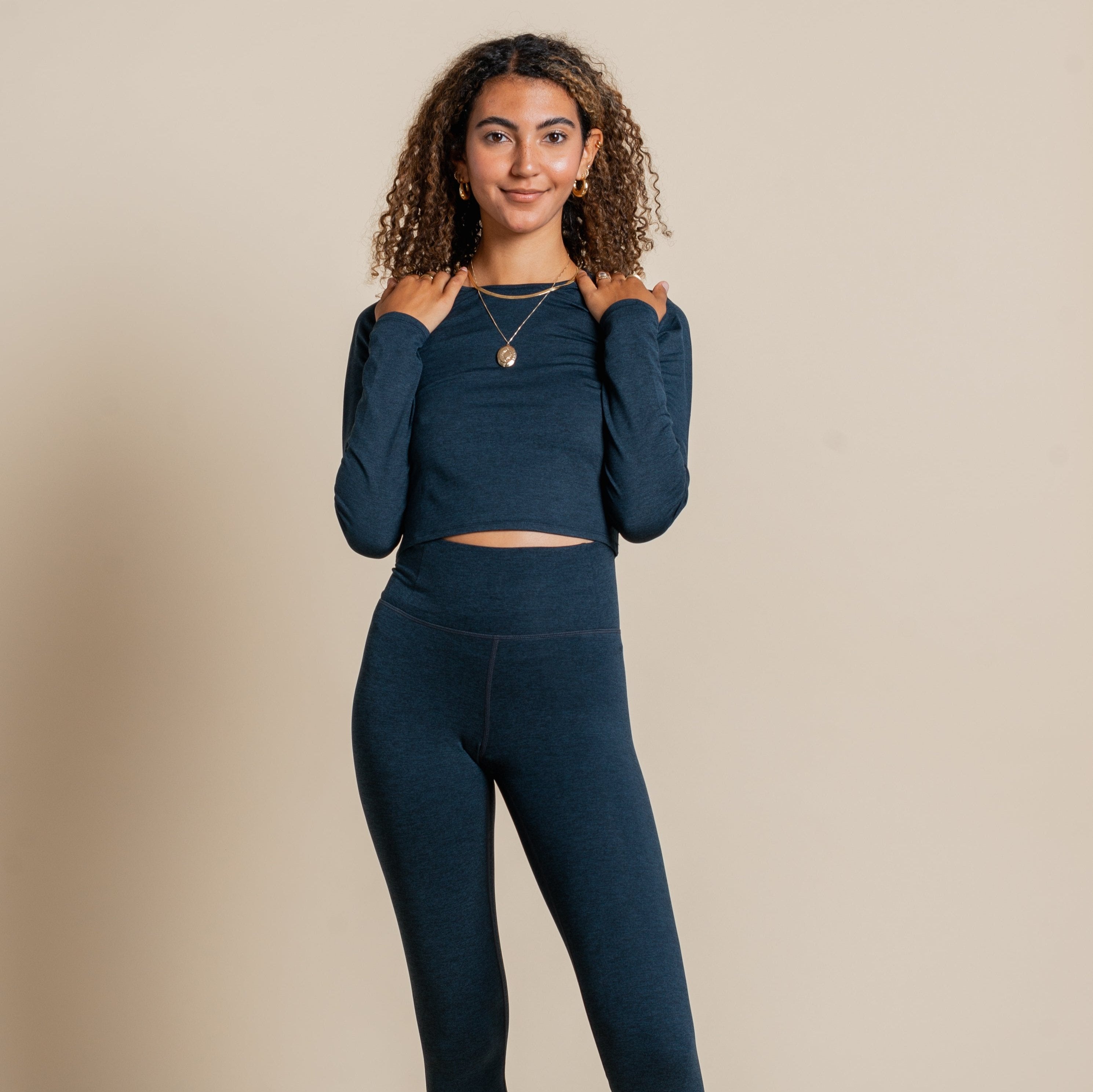 Frau in dunkelblauer Sportkleidung vor einem beigen Hintergrund schaut in die Kamera.