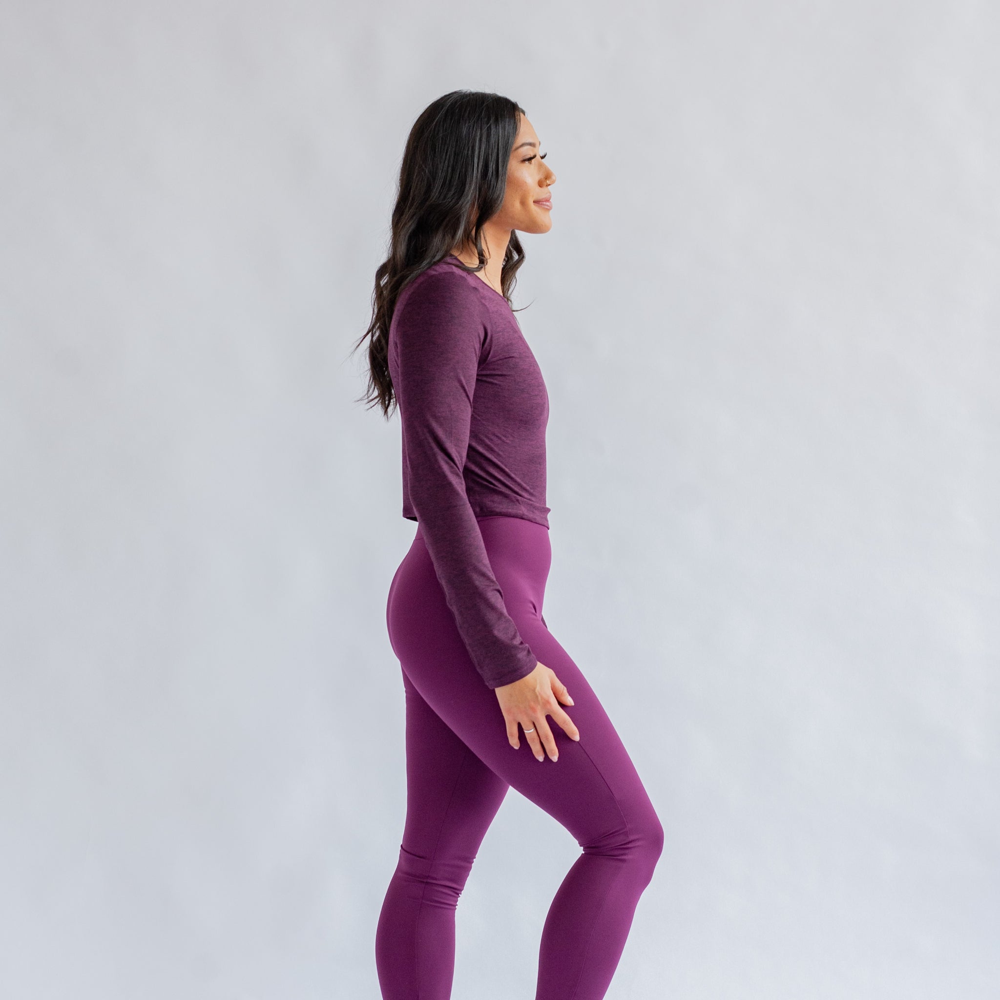 Frau in lilafarbener Sportkleidung steht seitlich vor einem grauen Hintergrund.