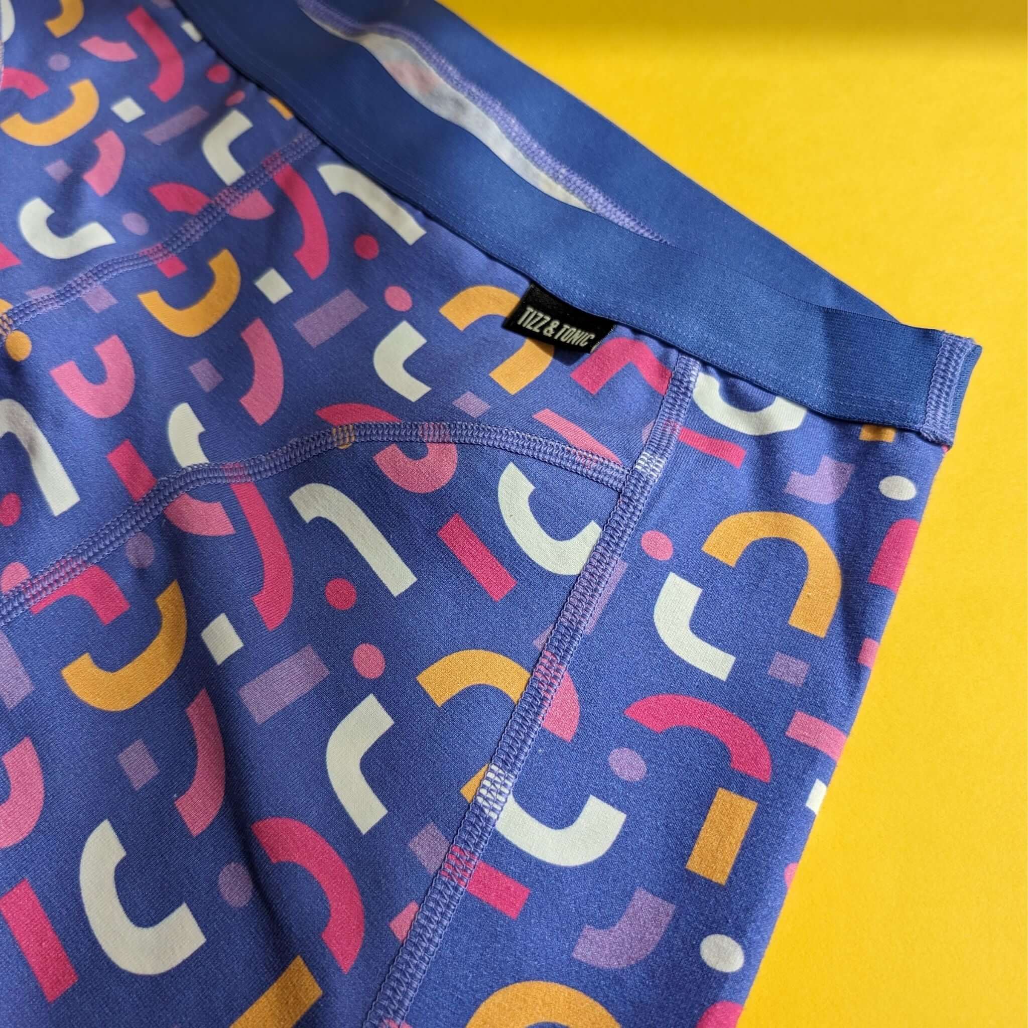 Bunte Leggings mit geometrischen Mustern auf blauem Stoff liegen auf einem gelben Hintergrund.