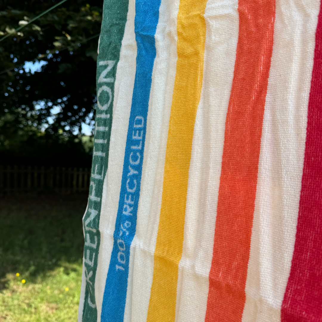 Bunte gestreifte Textilien mit der Aufschrift "GREEN PETITION 100% RECYCLED" hängen im Freien vor einem grünen Hintergrund.