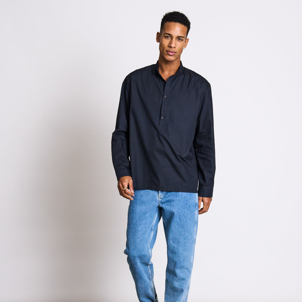 Mann in dunkelblauem Hemd und blauen Jeans steht vor einem weißen Hintergrund.