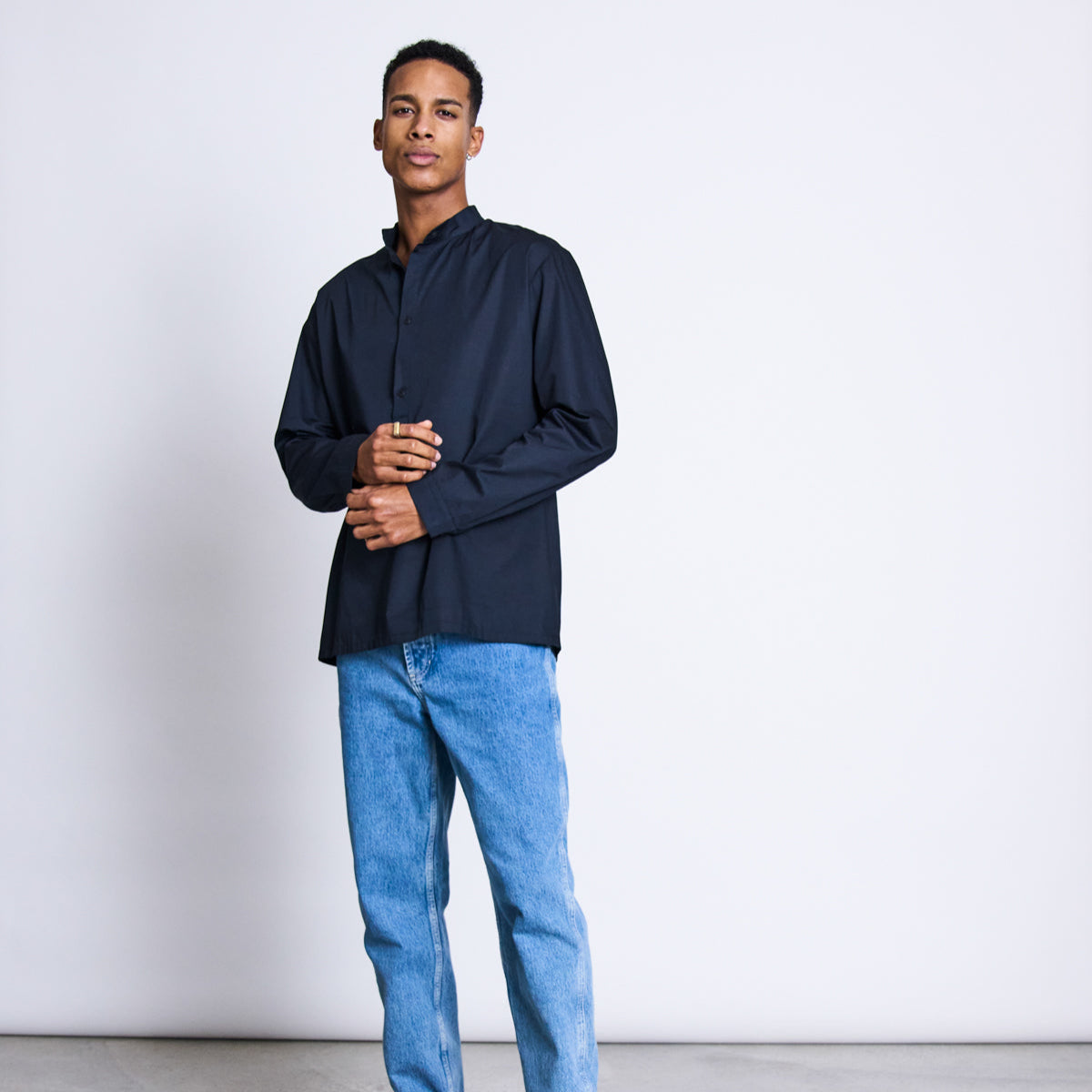 Ein Mann in einem dunkelblauen Hemd und blauen Jeans steht vor einem weißen Hintergrund.
