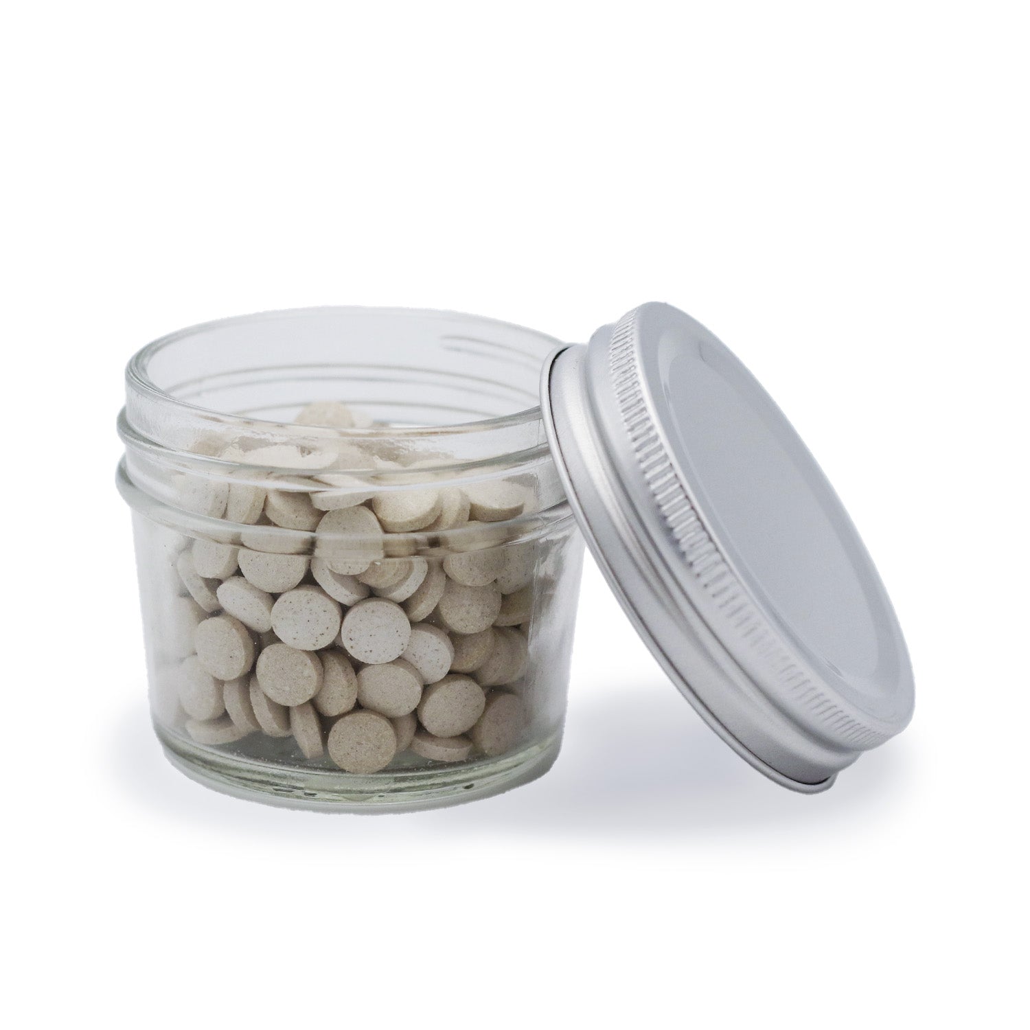 Glasgefäß mit weißlichen Tabletten und offenem Deckel auf weißem Hintergrund.