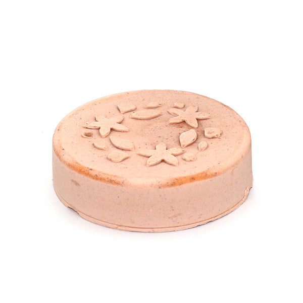 Runde Seife in Beige mit einem eingeprägten Blumenmuster auf weißem Hintergrund.