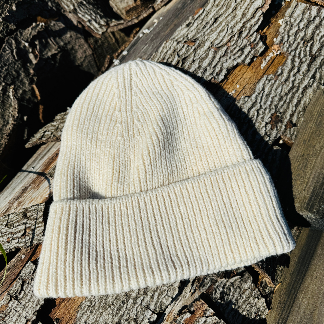 Beige Strickmütze liegt auf Baumrinde in der Sonne.
