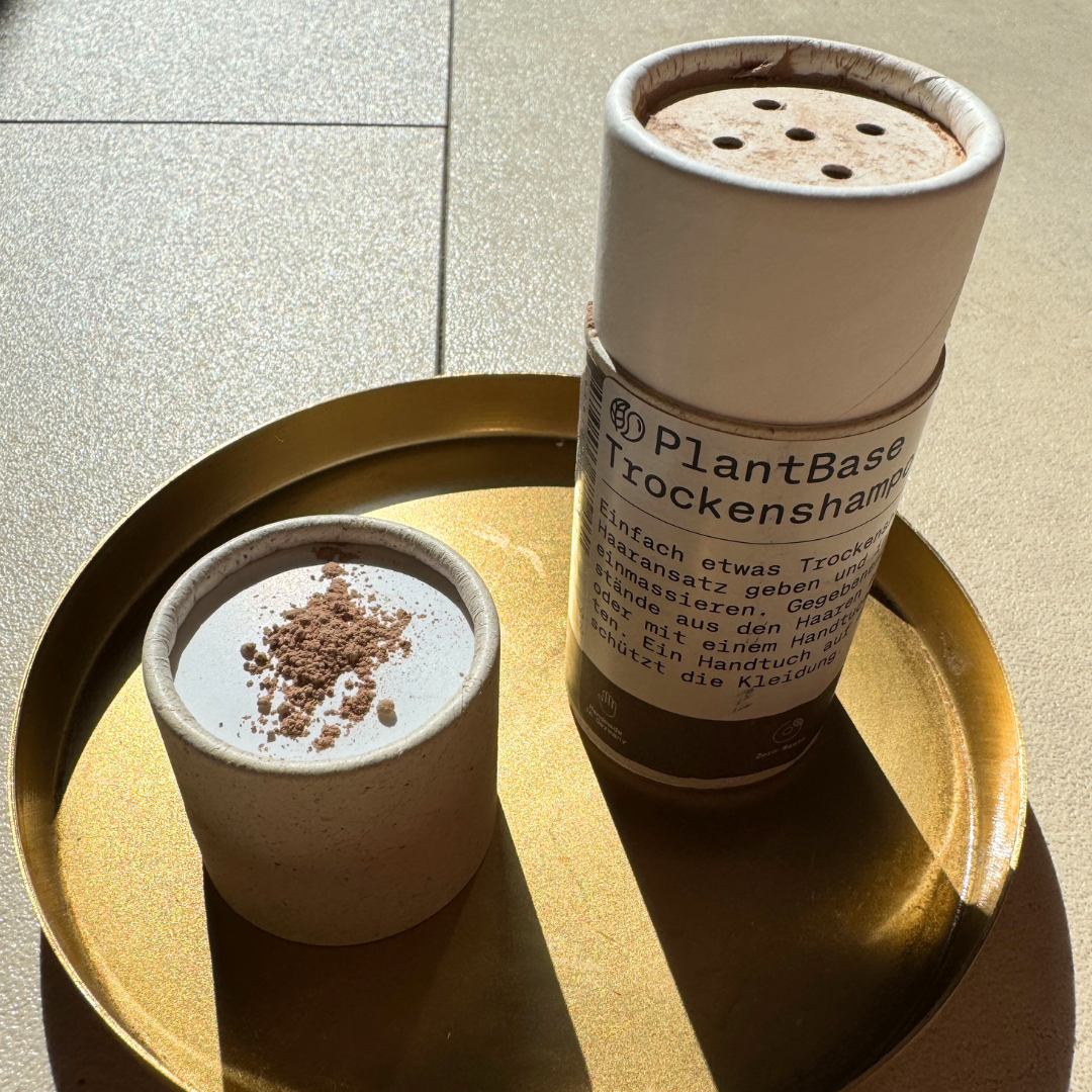 Zwei Behälter mit Trockenpulver und einer Packung Trocken-Shampoo auf einem goldenen Tablett in der Sonne.