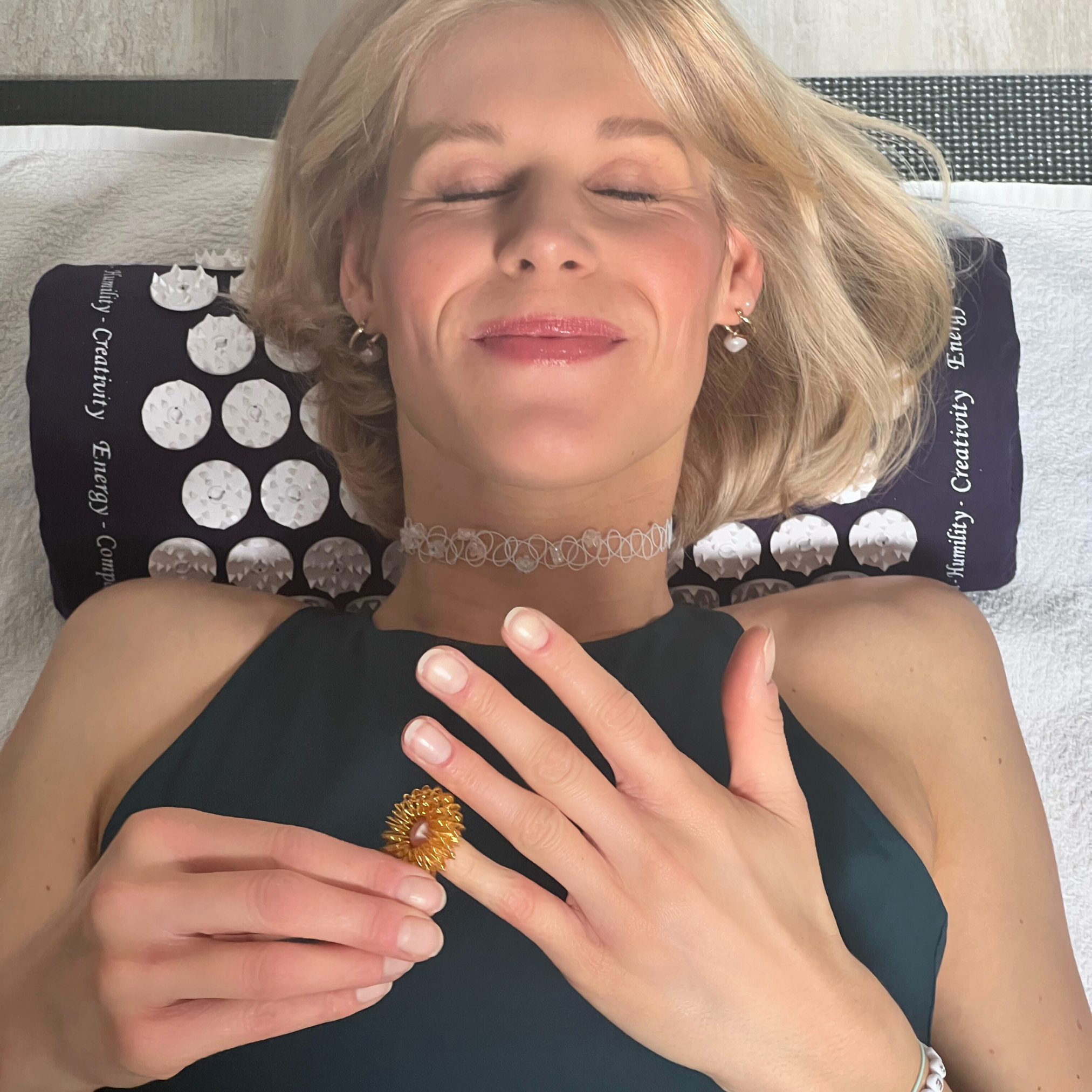 Frau liegt entspannt mit geschlossenen Augen auf einem Polster und hält einen stacheligen Ring in der Hand.